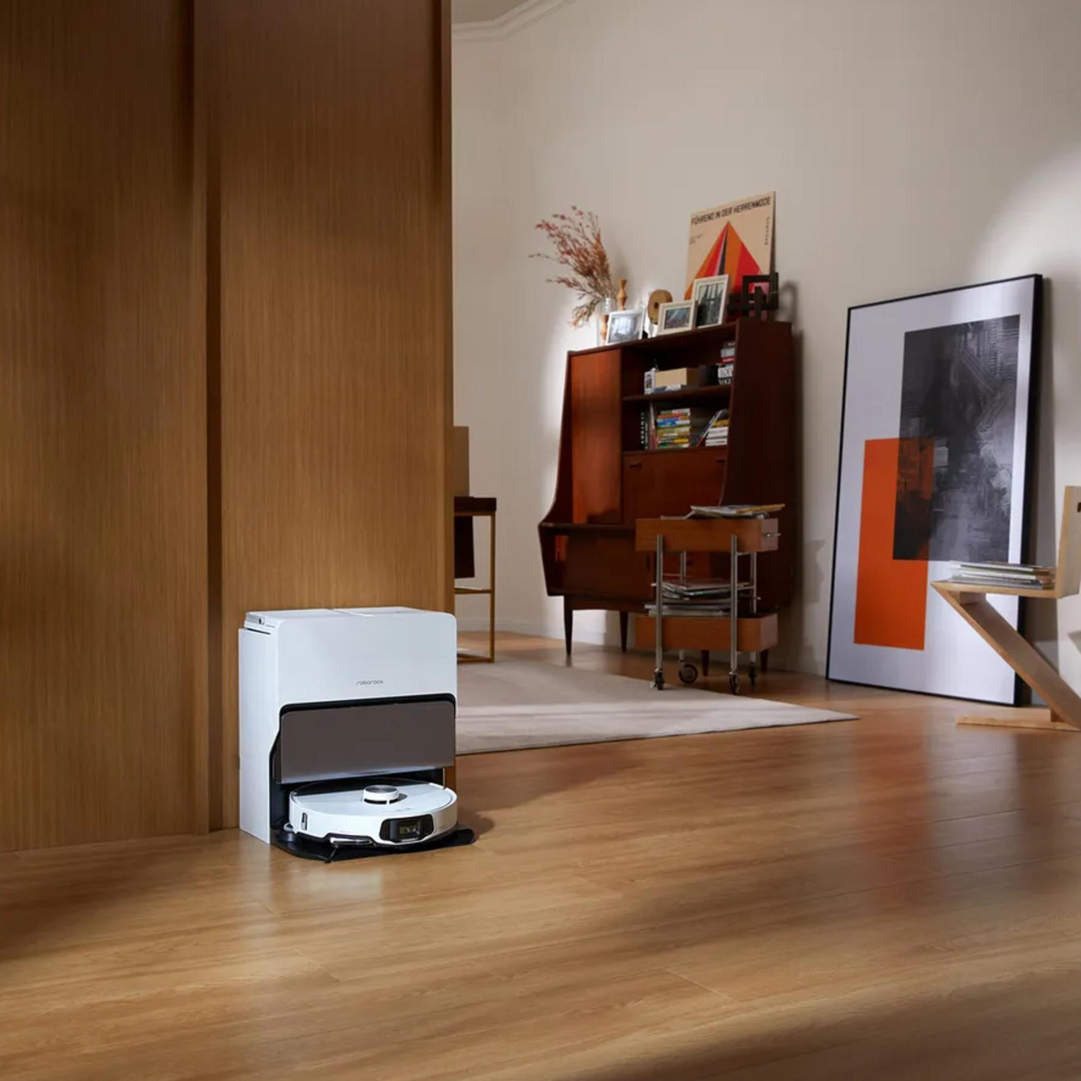 Biały robot sprzątający stoi w stacji ładującej na drewnianej podłodze.