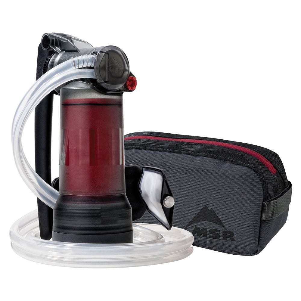 Ein Wasserfilter mit rotem Behälter, schwarzem Griff und Schlauch neben einer grauen Tasche.