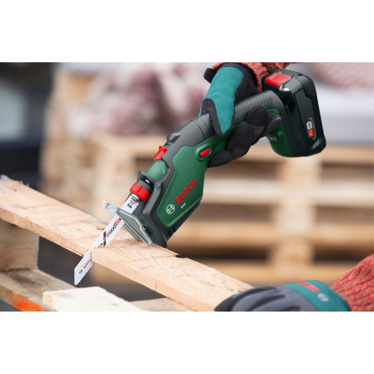 Eine Person in Handschuhen benutzt eine kabellose Bosch-Säge zum Schneiden eines Holzbretts auf einer Palette.