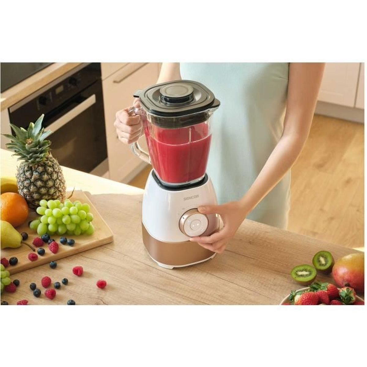 Eine Frau benutzt einen Mixer mit rotem Saft und frischem Obst daneben.