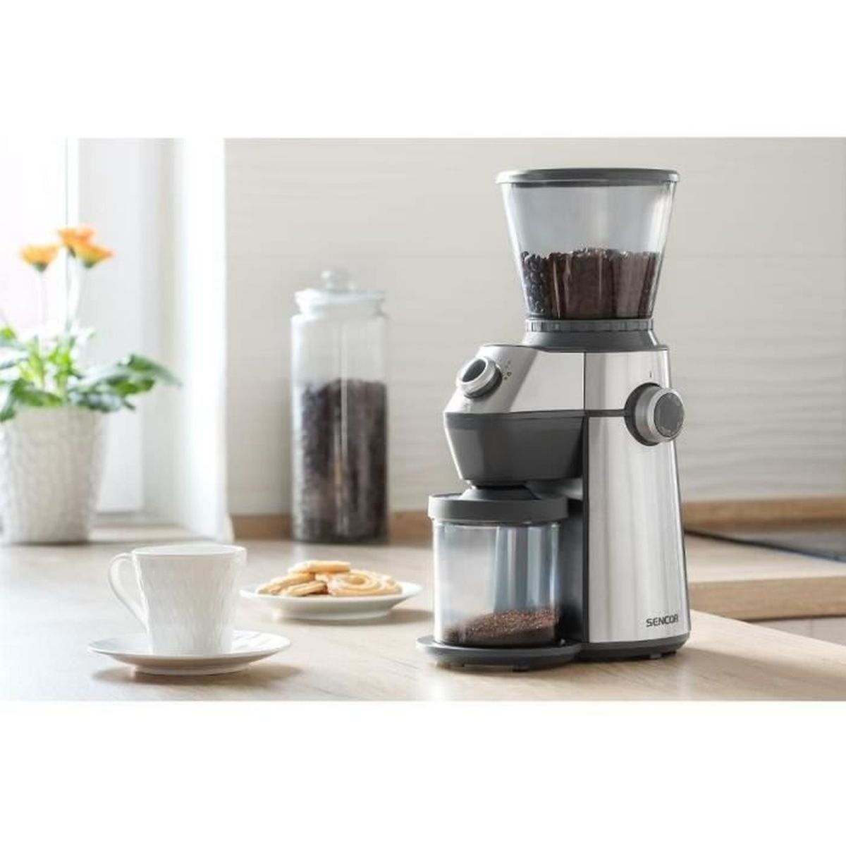 Kaffeemühle mit Bohnenbehälter, Kaffeetasse und Keksen auf Holztisch.