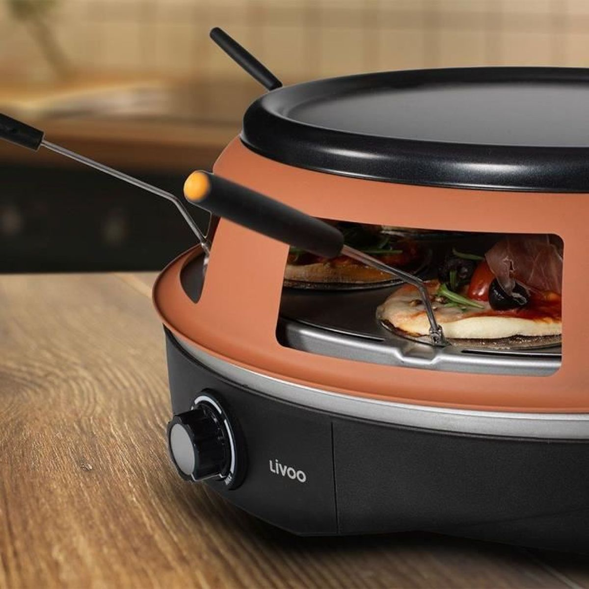 Un forno per pizza color rame con due piccole pizze all'interno, su un tavolo di legno.