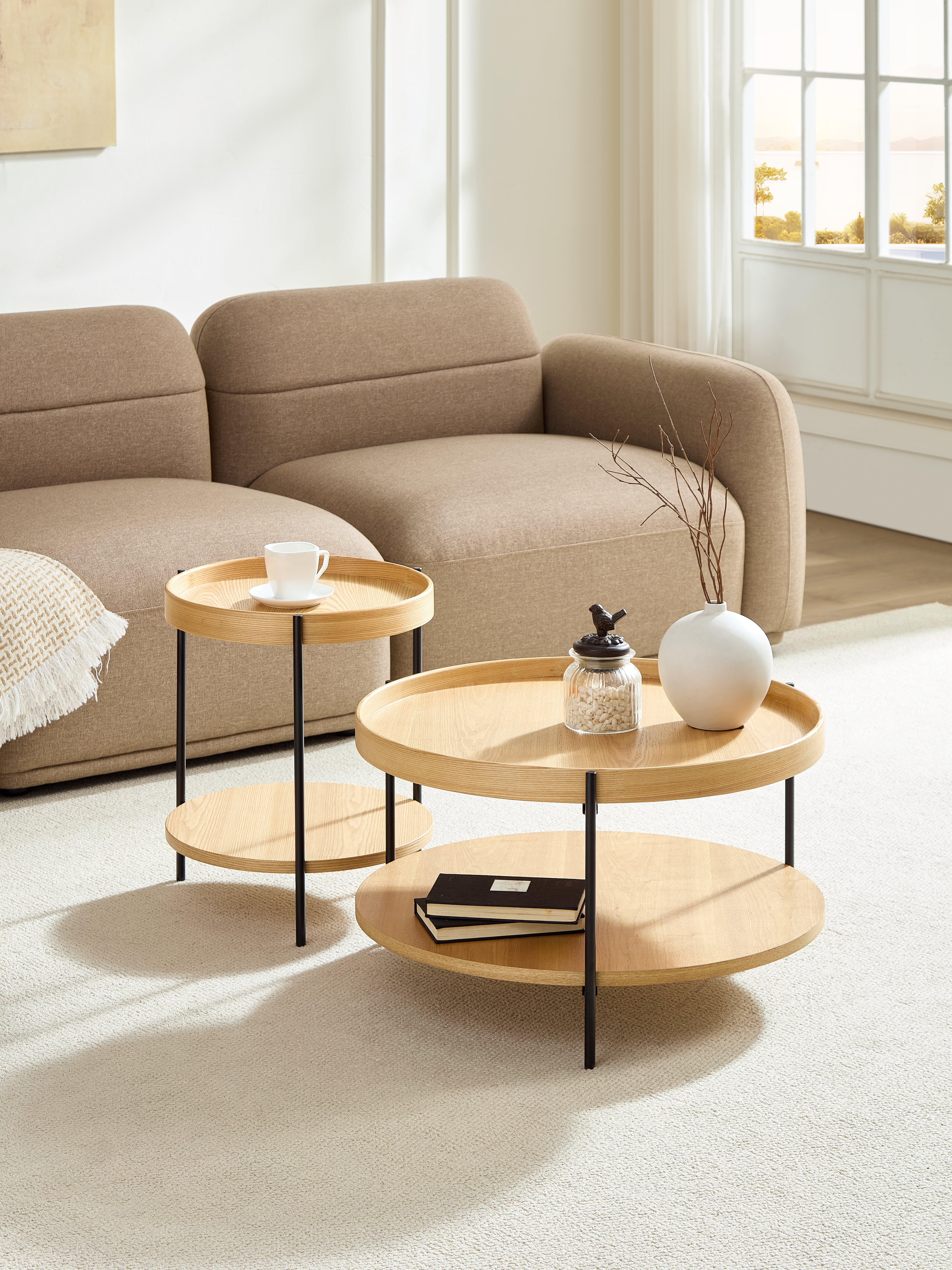 Ein braunes Sofa mit zwei runden Holztischen. Einer hat eine Tasse, der andere Bücher.