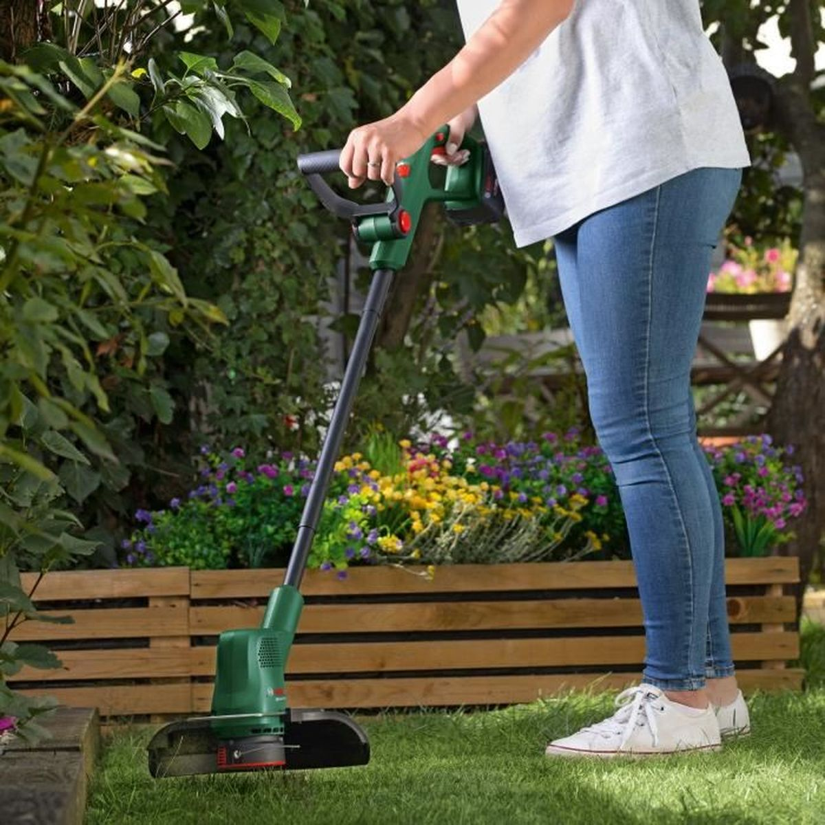 Eine Person trimmt mit einem grünen Rasentrimmer Gras in einem Garten.