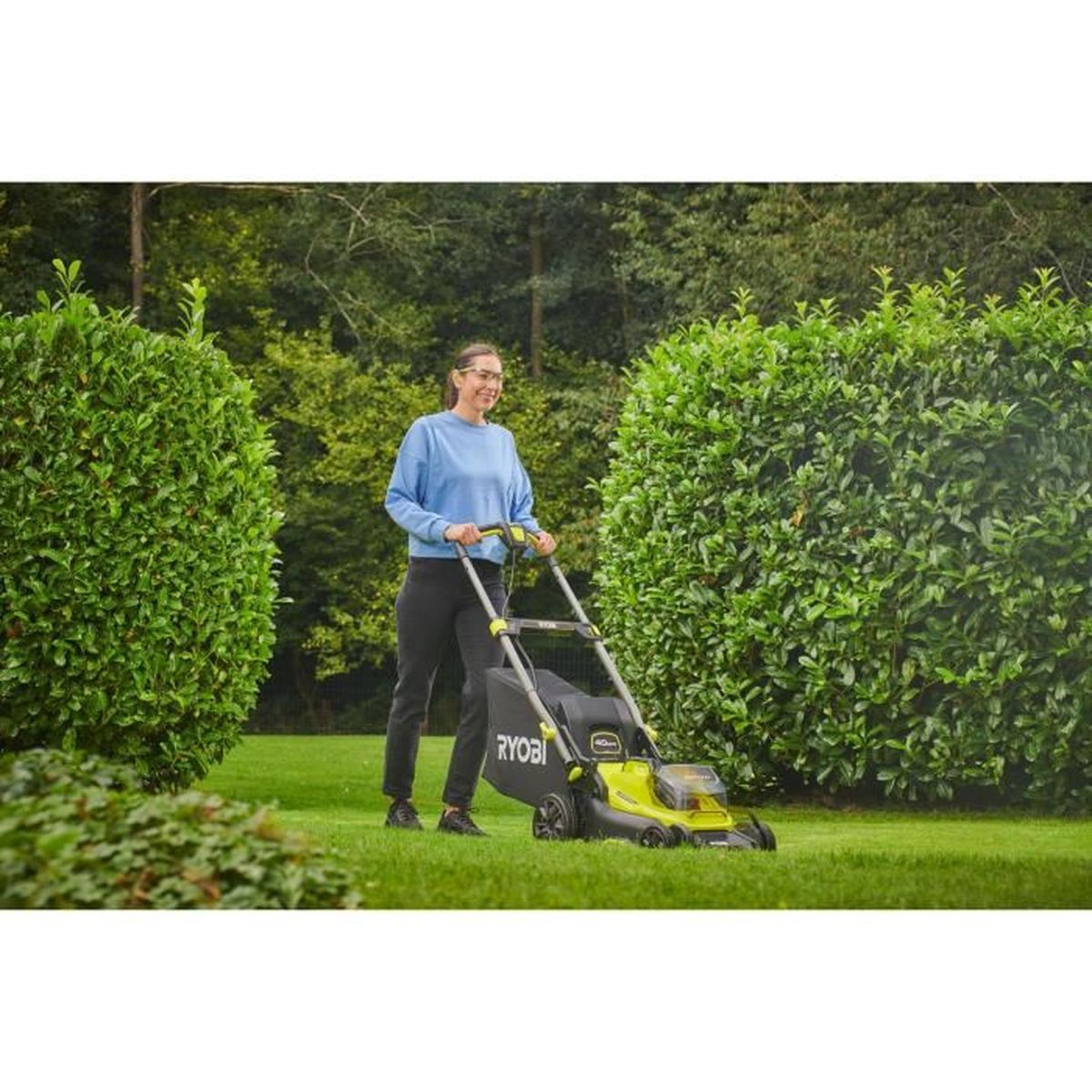 Eine Frau mäht mit einem Rasenmäher im Garten den Rasen.