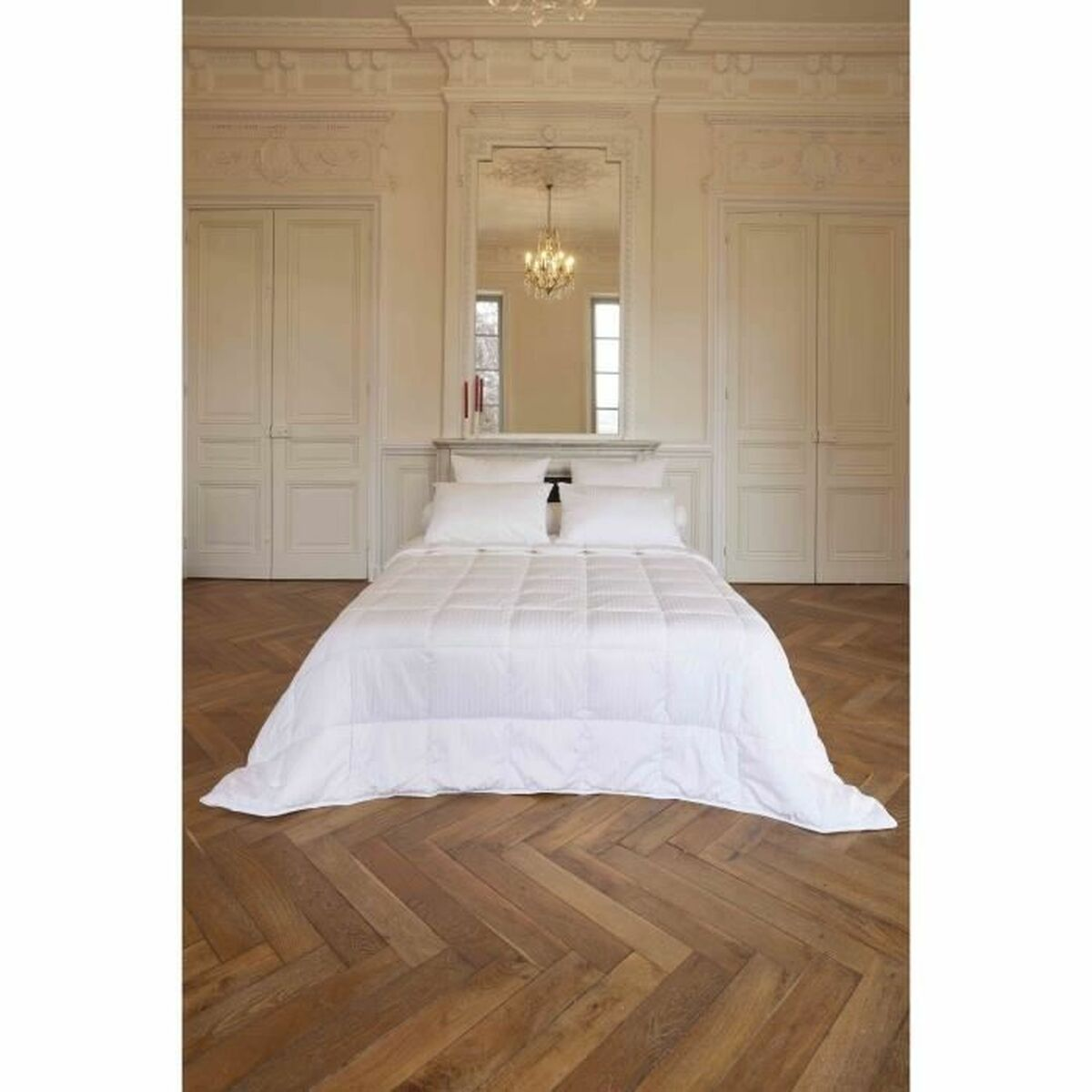 Ein weißes Bett mit Decke und Kissen steht auf einem Holzboden.
