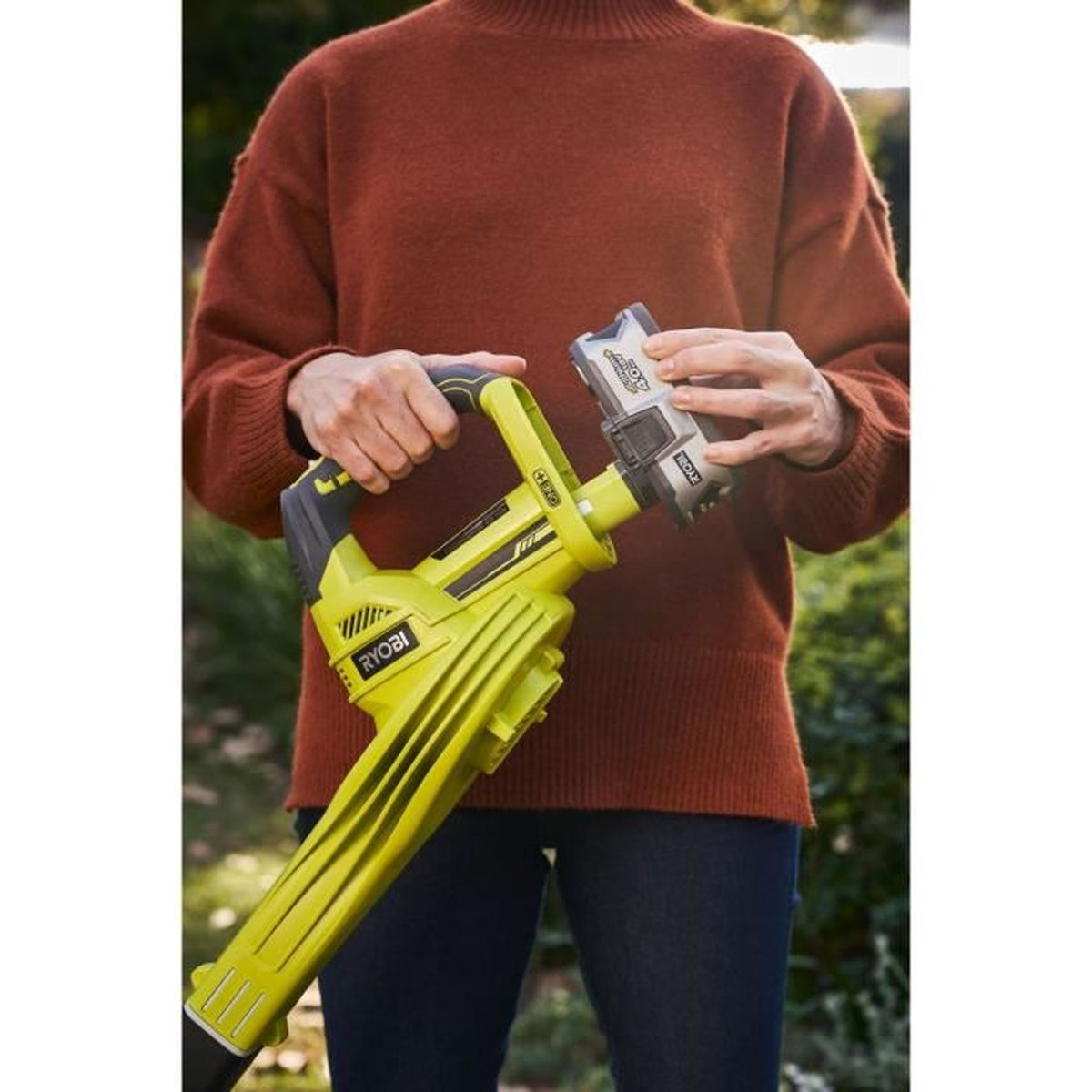Persona che tiene un soffiatore per foglie Ryobi verde, inserisce la batteria.