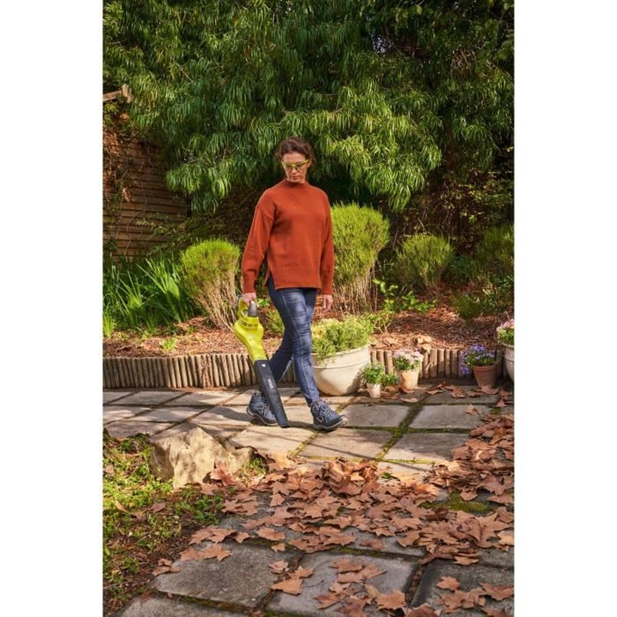 Donna con soffiatore nel giardino su sentiero in pietra con foglie.