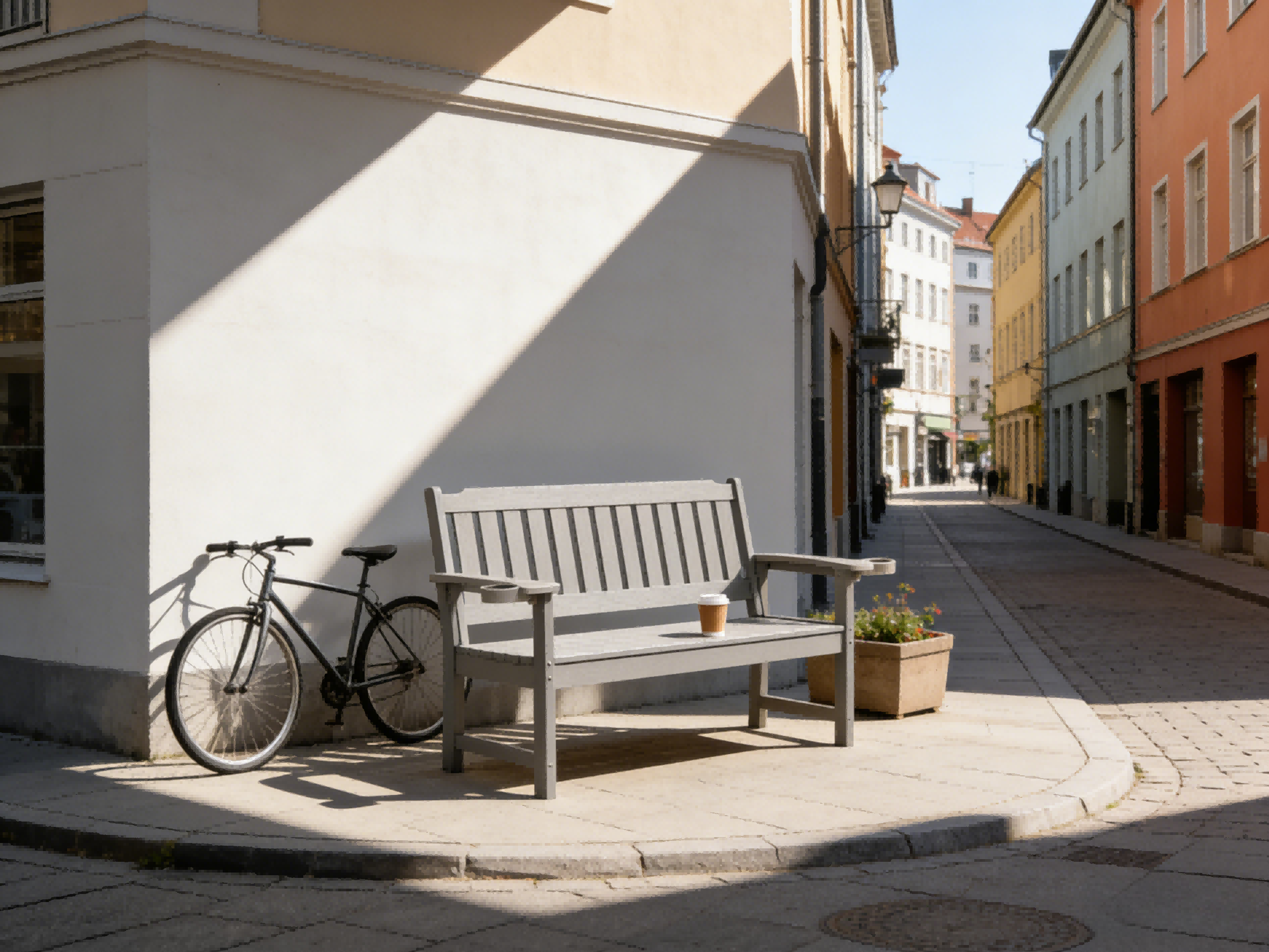 Eine graue Bank und ein Fahrrad stehen an einer sonnigen Straßenecke mit Gebäuden im Hintergrund.