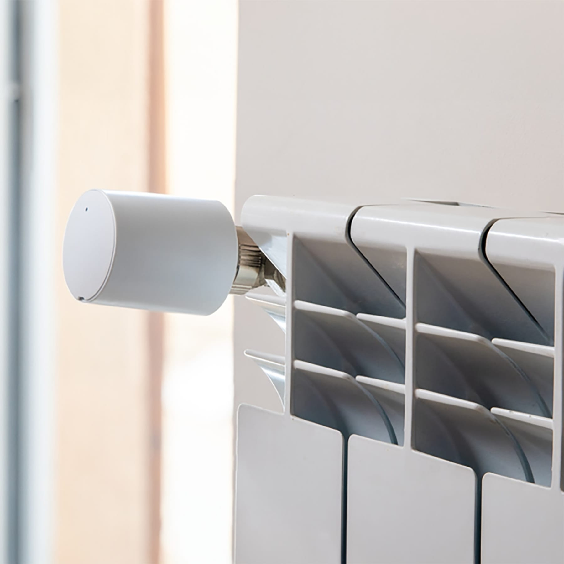 Biały termostat jest przymocowany do białego grzejnika. Rozmyte tło.