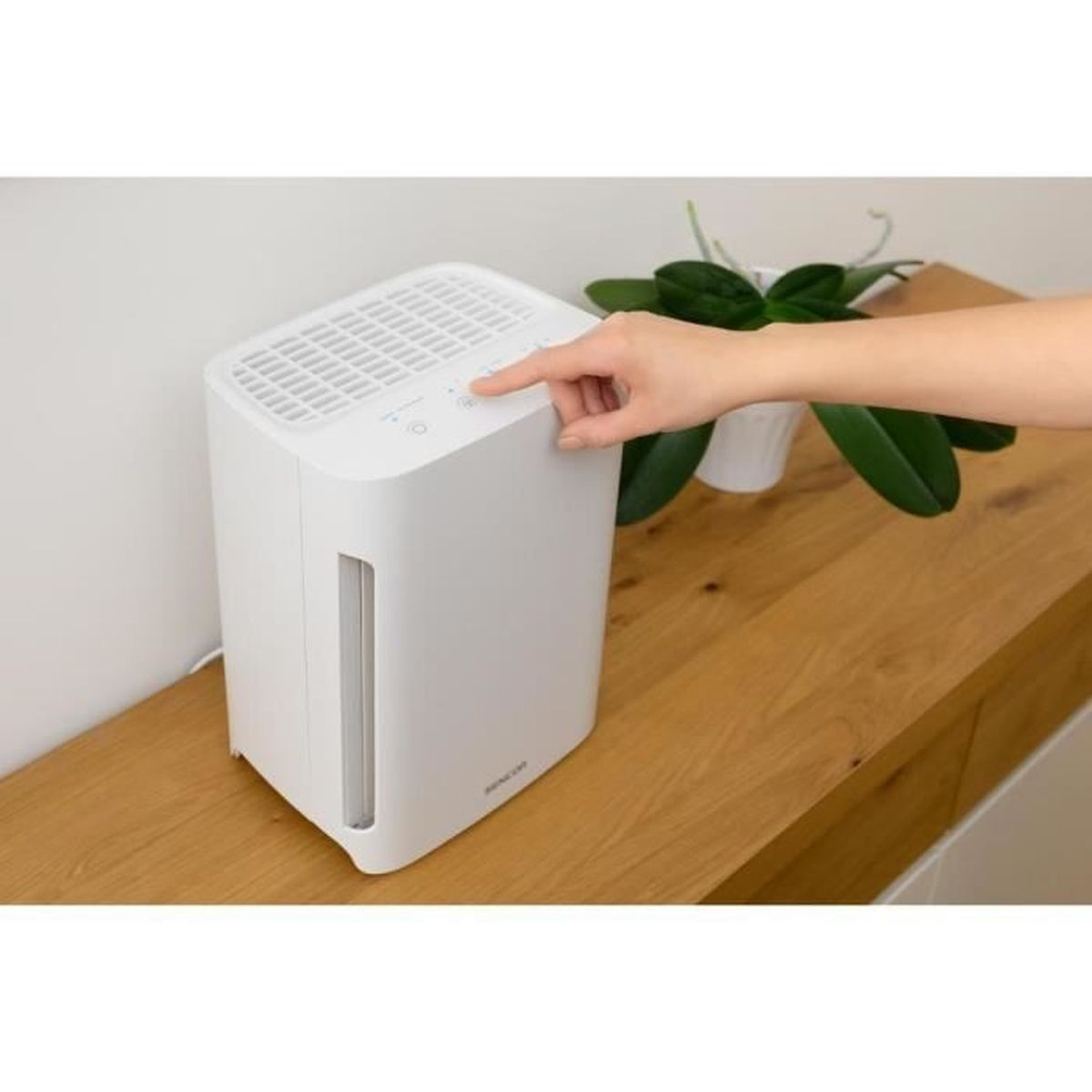 Un purificatore d'aria bianco su un tavolo di legno, con una mano che preme un pulsante.