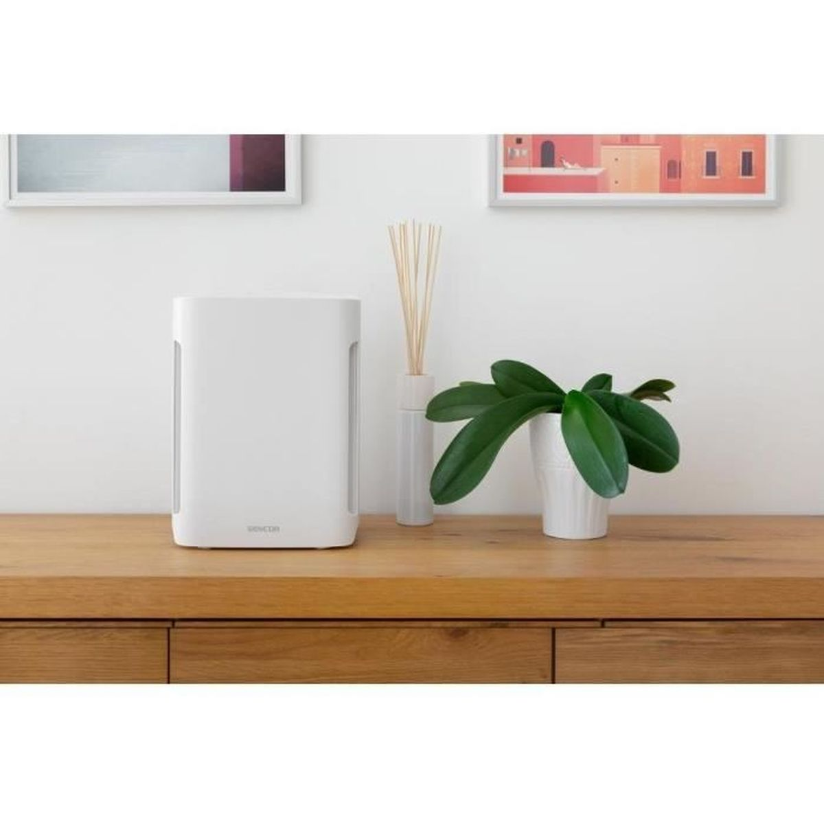 Un purificatore d'aria bianco accanto a un'orchidea e bastoncini diffusori.