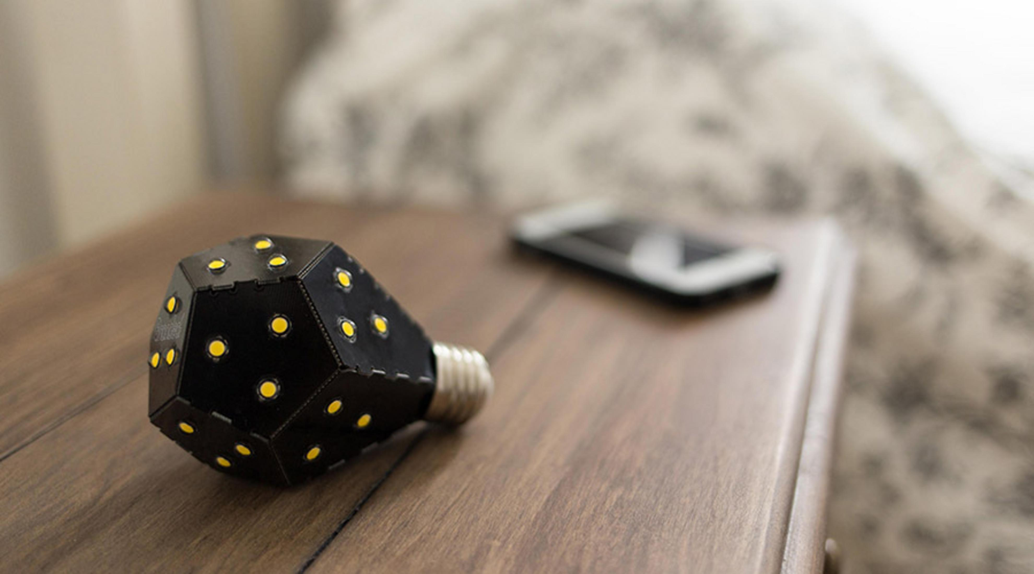 Czarna lampa z żółtymi światłami leży na szafce nocnej obok smartfona.