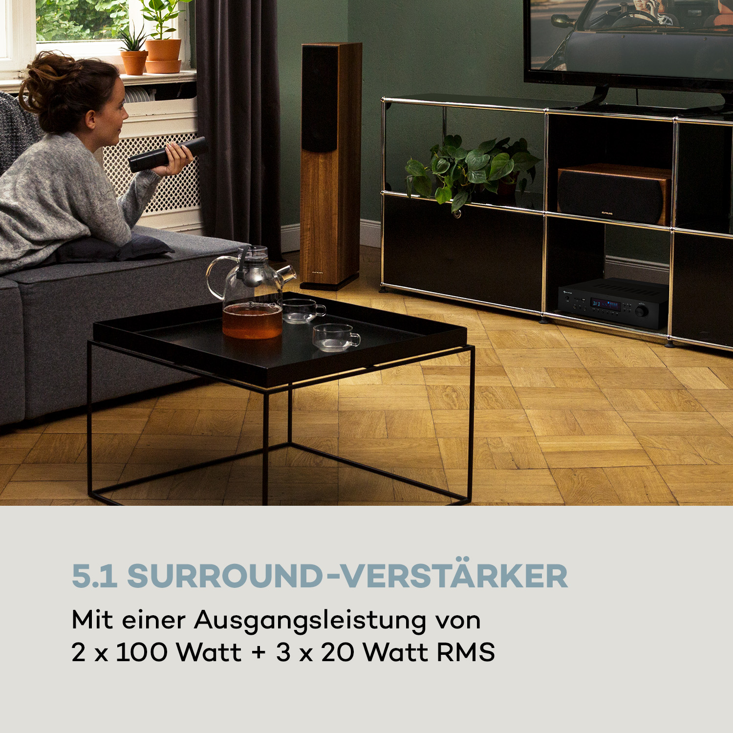 Frau auf Sofa mit Fernbedienung, Lautsprecher, Tisch mit Teekanne.