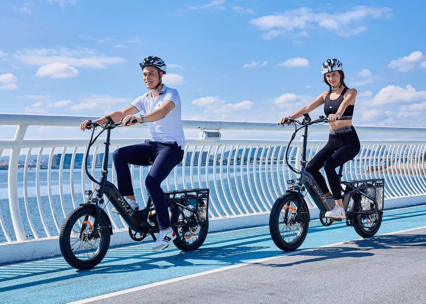 Dos personas montan bicicletas eléctricas en un puente bajo cielo azul.