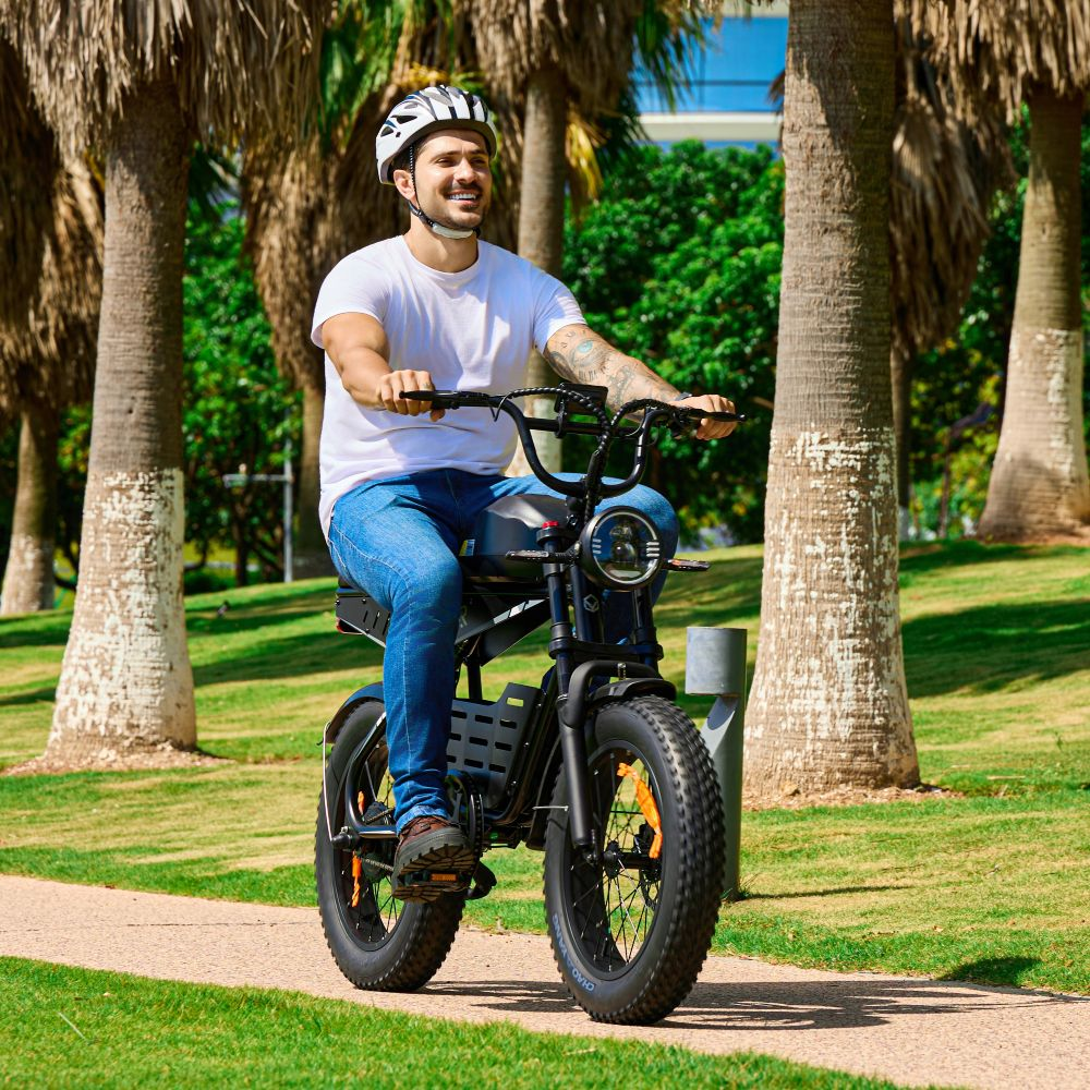 Un hombre monta una bicicleta eléctrica por un camino con palmeras.