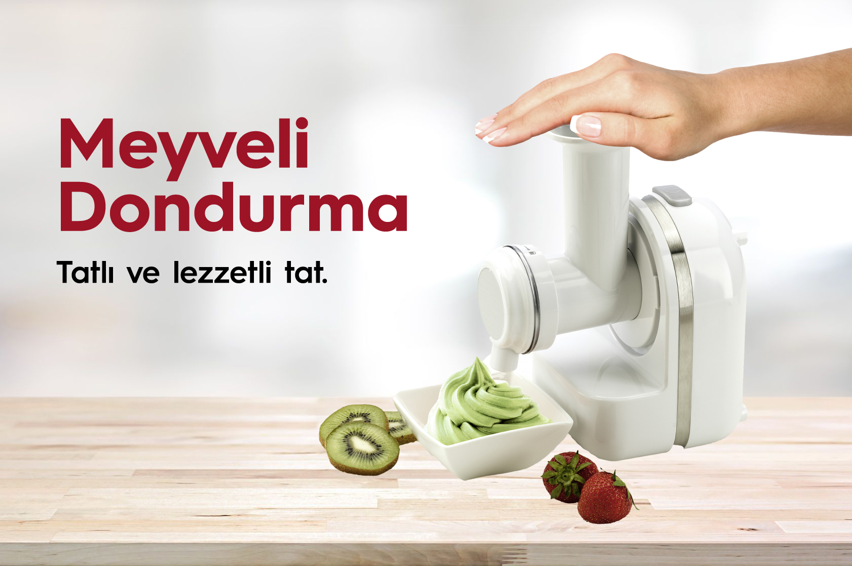 Bir el dondurma makinesi kullanıyor. Yeşil dondurma kaseye akıyor. Yanında kivi dilimleri ve çilek.