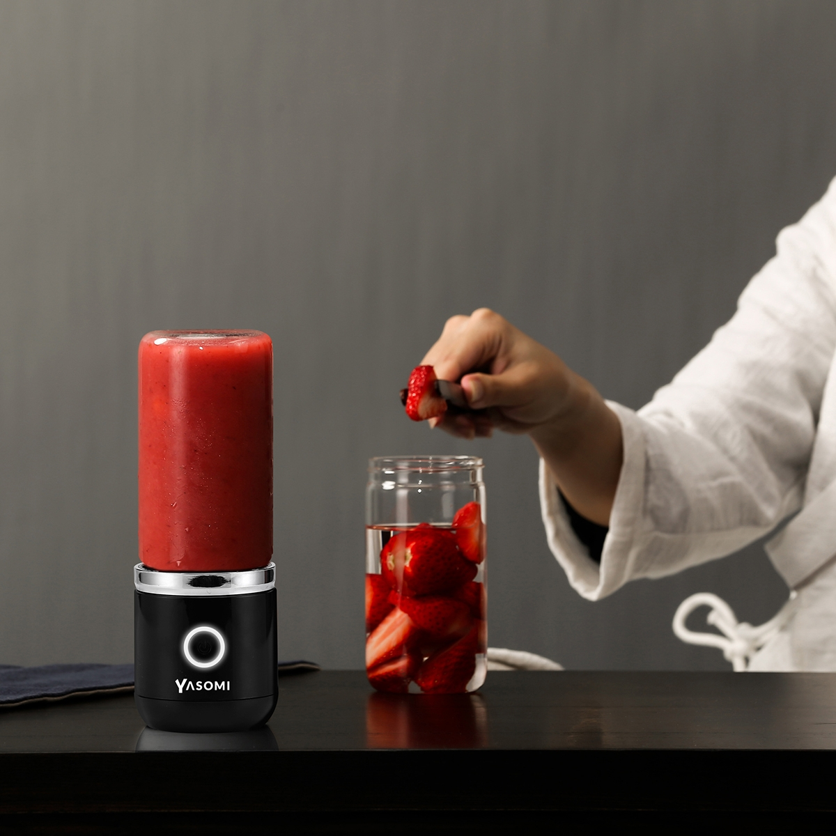 Kırmızı smoothie ve bardakta çilek bulunan siyah taşınabilir blender.