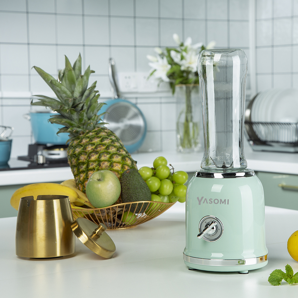 Nane yeşili blender, ananas, elma, üzüm ve avokado içeren bir meyve kasesinin yanında.