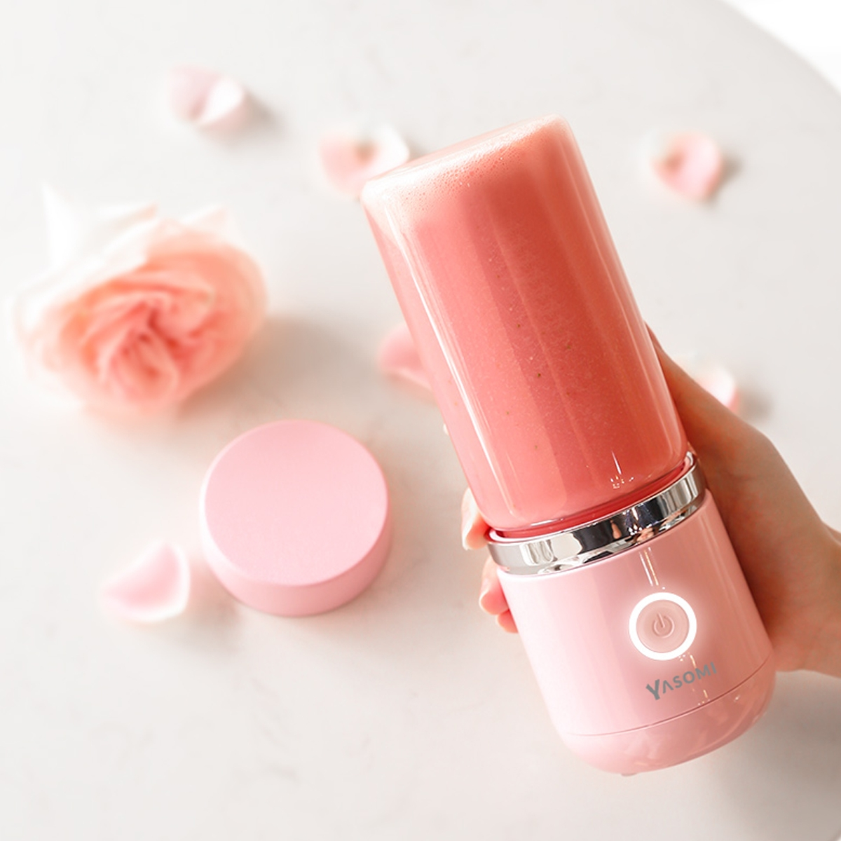 Pembe meyveli pembe blender ve gül yaprakları bir el tarafından tutuluyor.