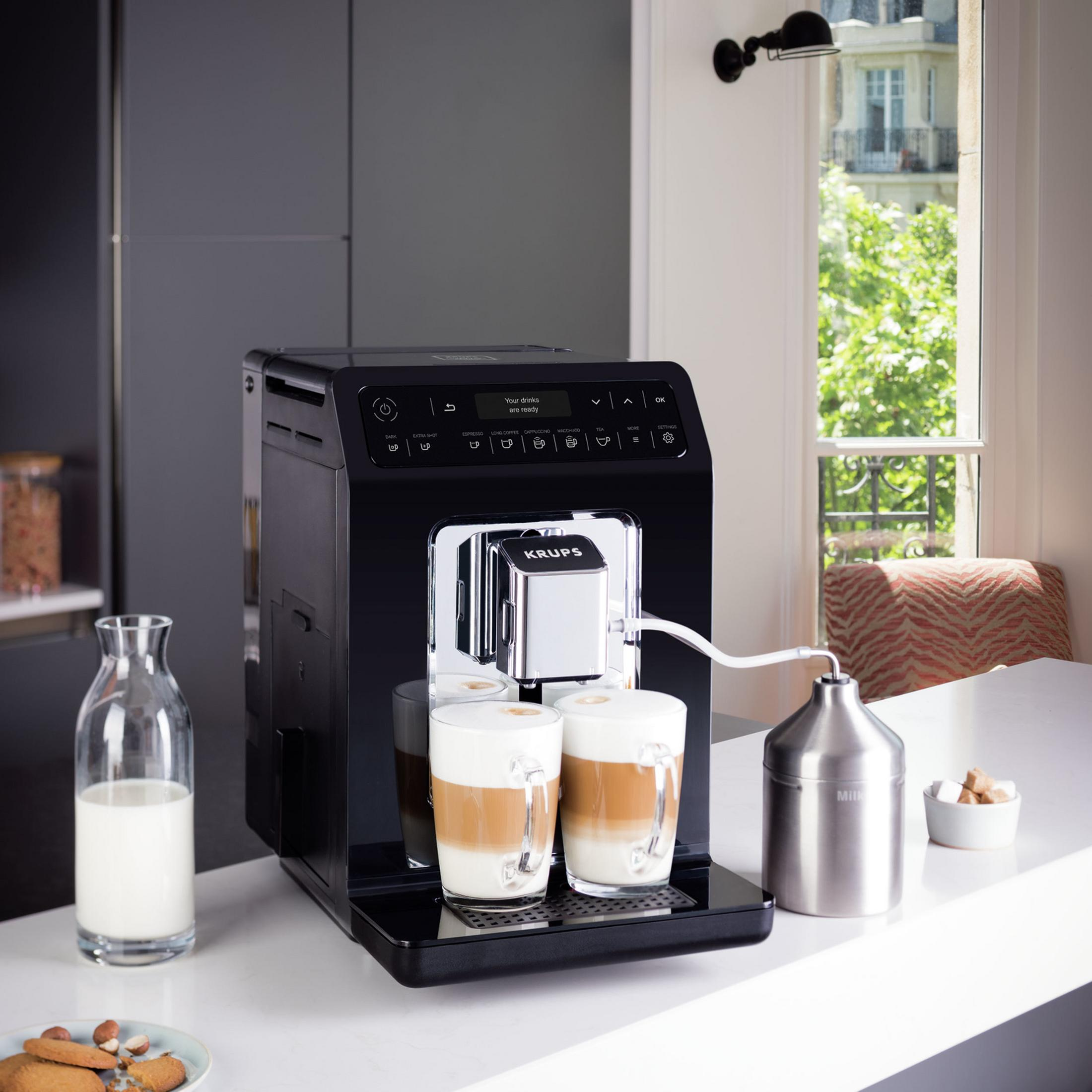 Ekspres do kawy z dwoma gotowymi latte, butelką mleka i ciasteczkami.