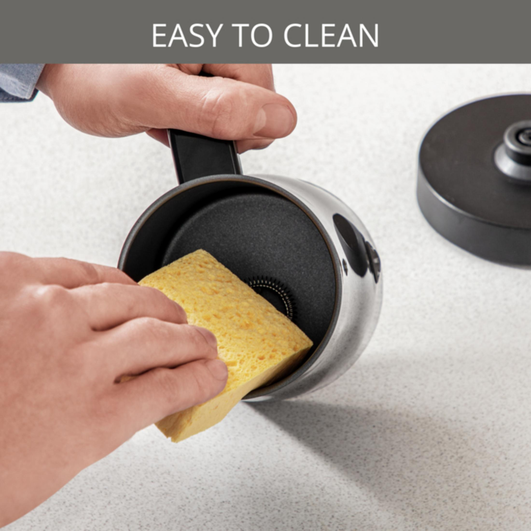 Dłoń czyści wnętrze czajnika z żółtą gąbką.