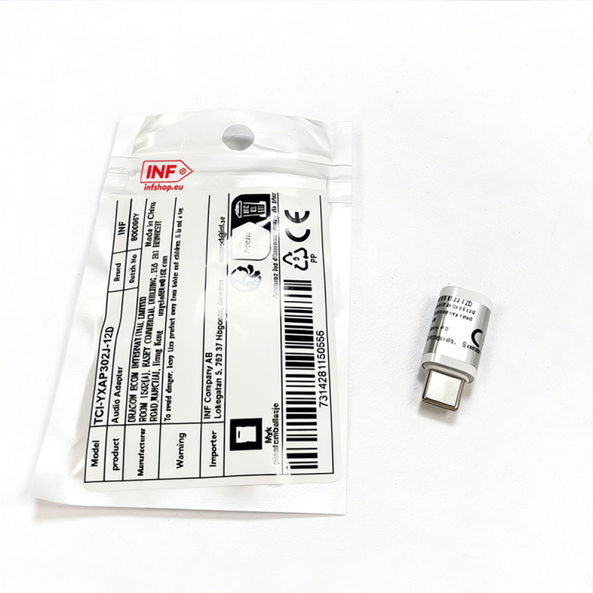 Srebrny adapter USB-C leży obok opakowania z informacjami o produkcie.