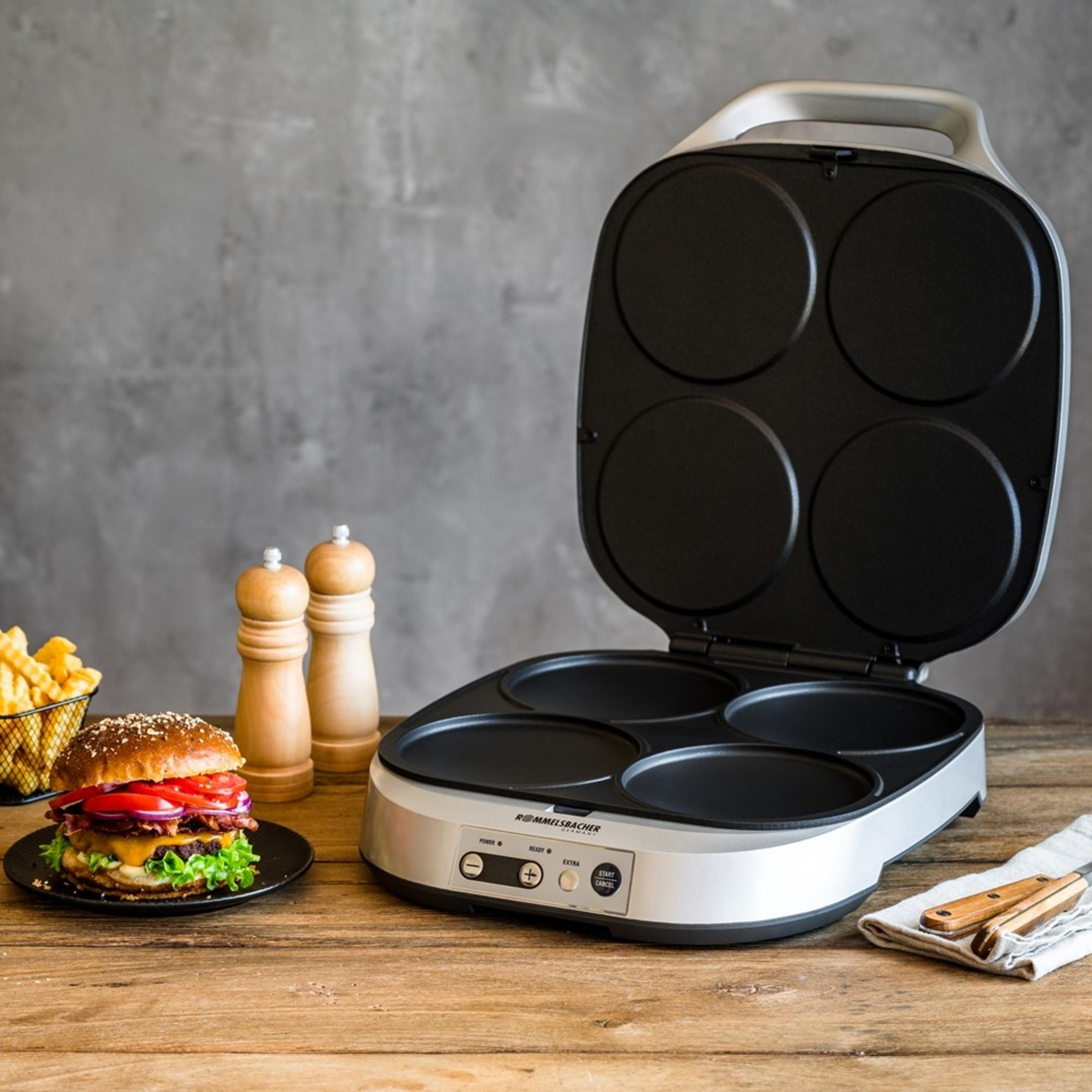 Otwarty grill płytowy z czterema okrągłymi wgłębieniami. Obok burger i frytki.