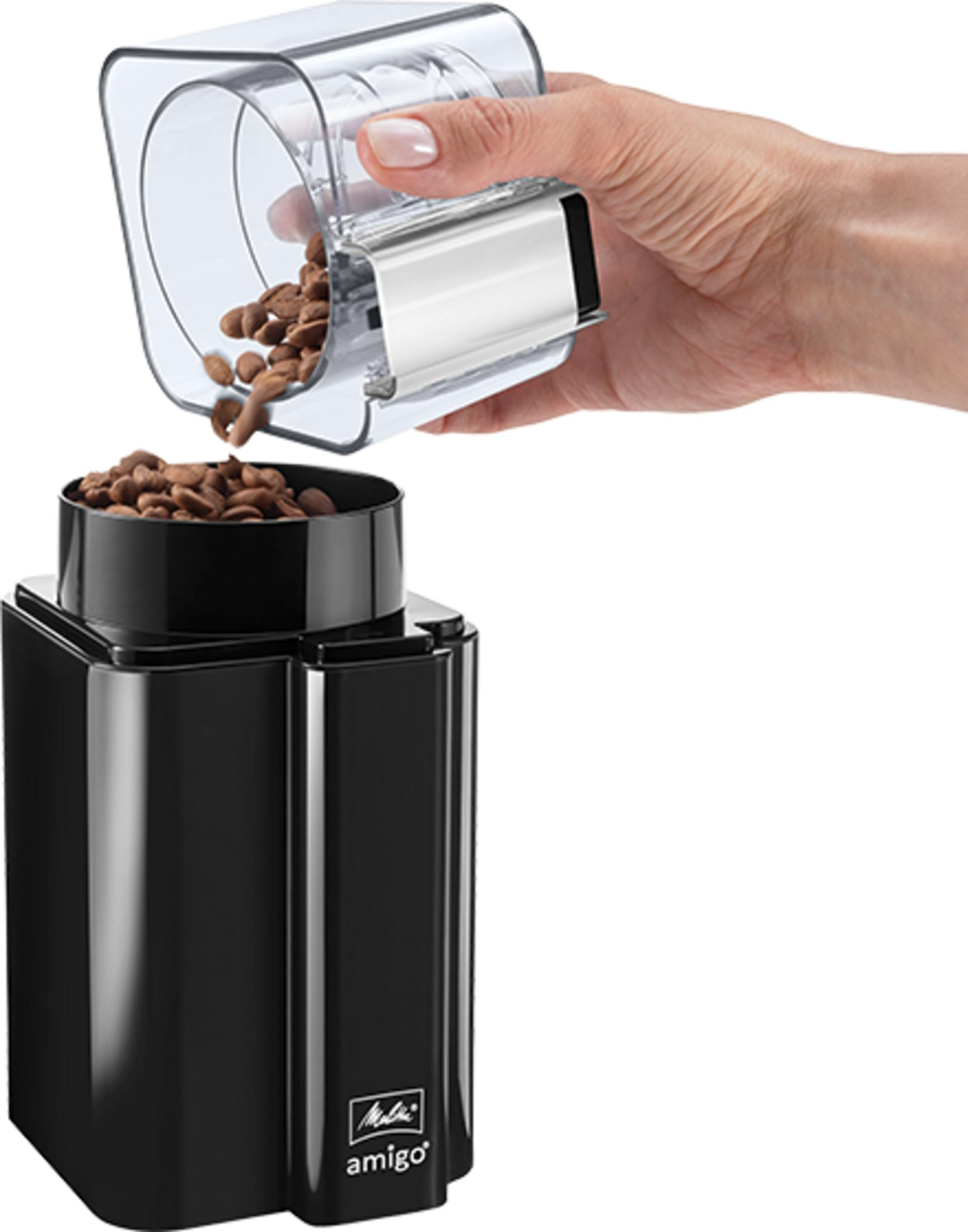 Ręka wsypuje ziarna kawy z przezroczystego pojemnika do czarnej nasadki młynka.