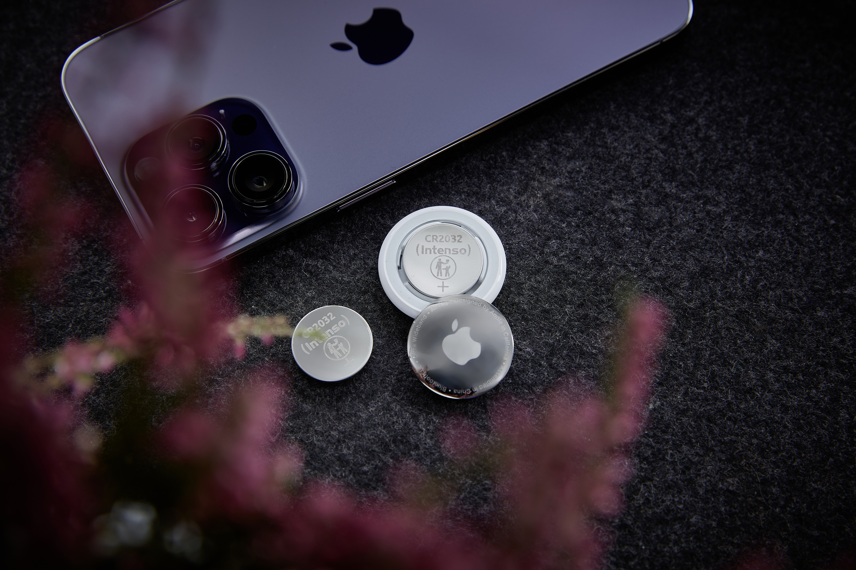 Fioletowy iPhone leży obok dwóch baterii CR2032 i lokalizatora AirTag.