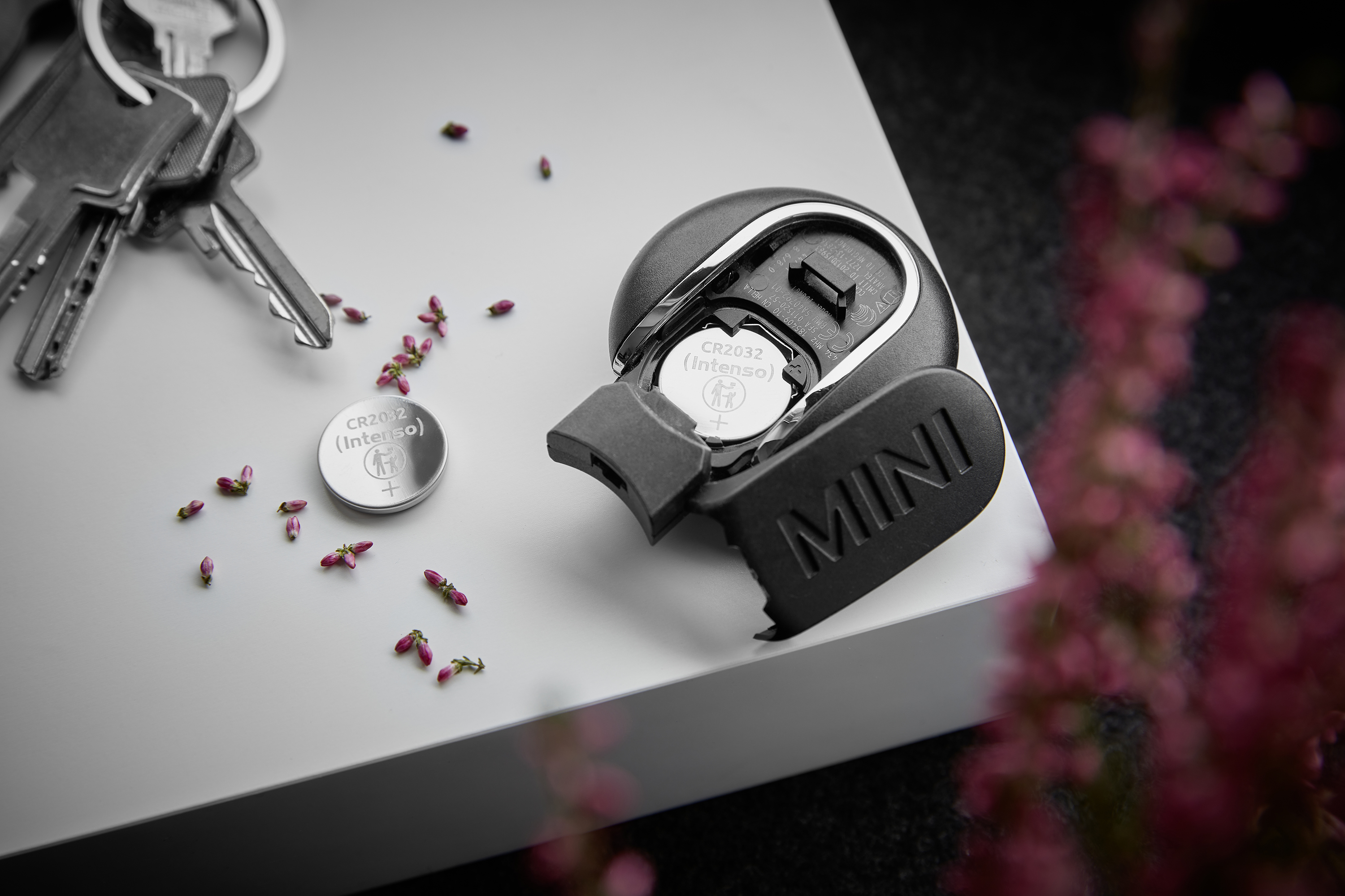 Kluczyk samochodowy Mini leży z bateriami i kwiatami na powierzchni.