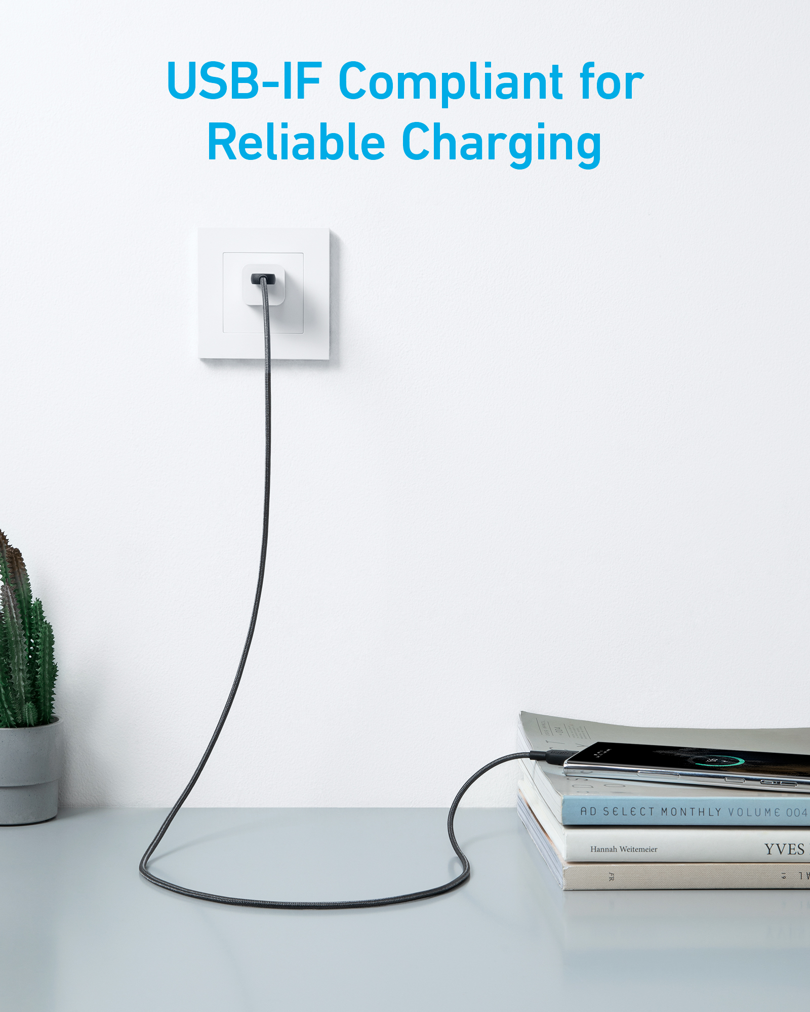 Un câble USB gris est branché à une prise, un téléphone charge sur des livres.