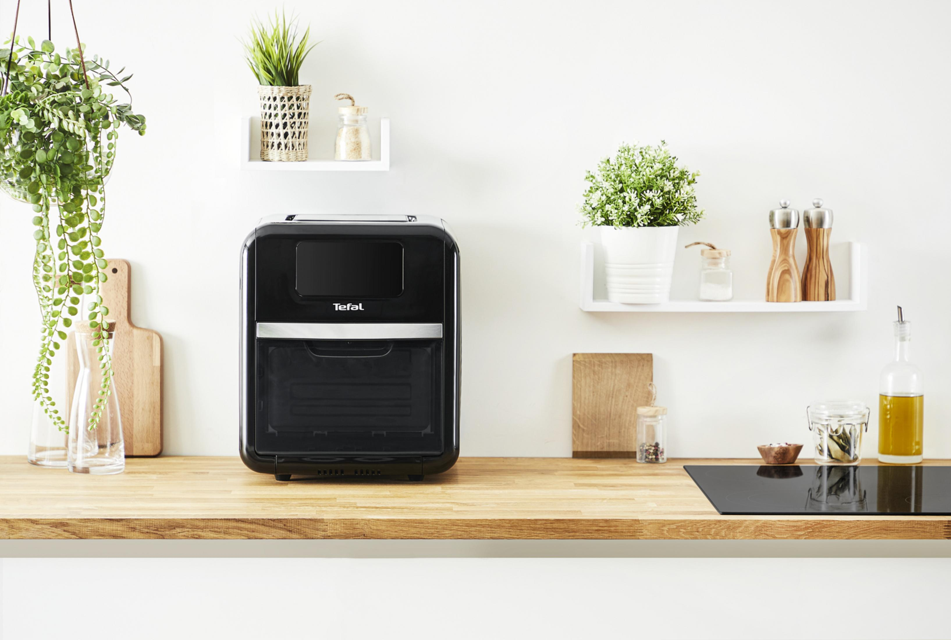 Czarna frytkownica Tefal na drewnianym blacie z roślinami i przyprawami.