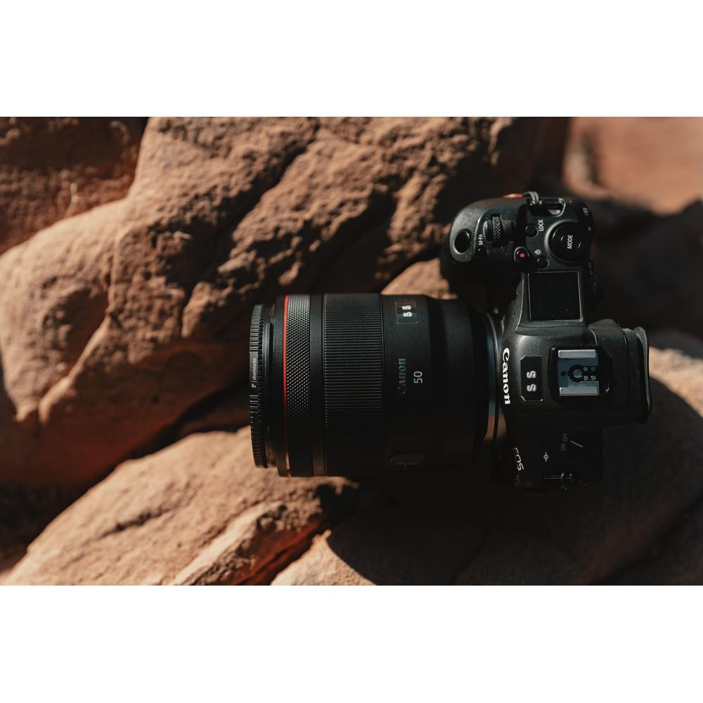 A black Canon camera with a 50mm lens rests on tan rocks.