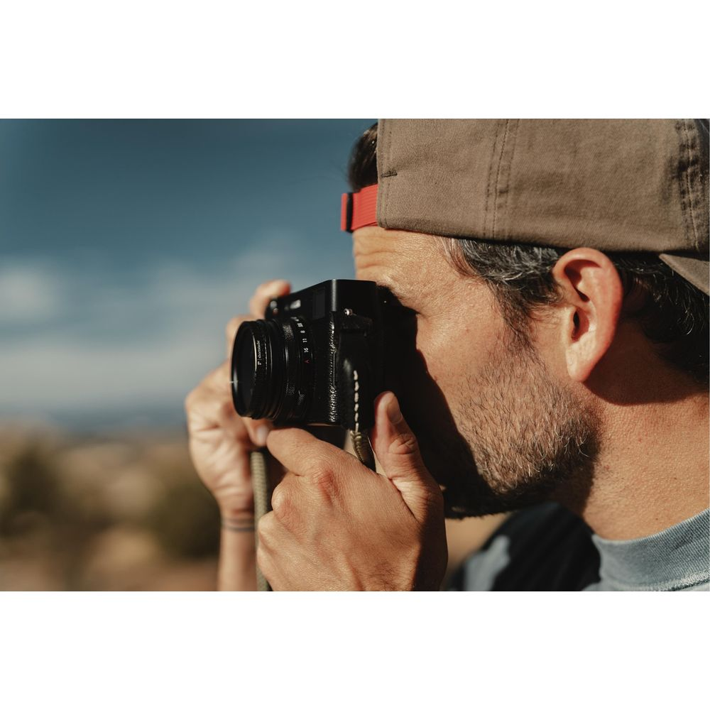 Man wearing a cap takes a photo with a camera outdoors.
