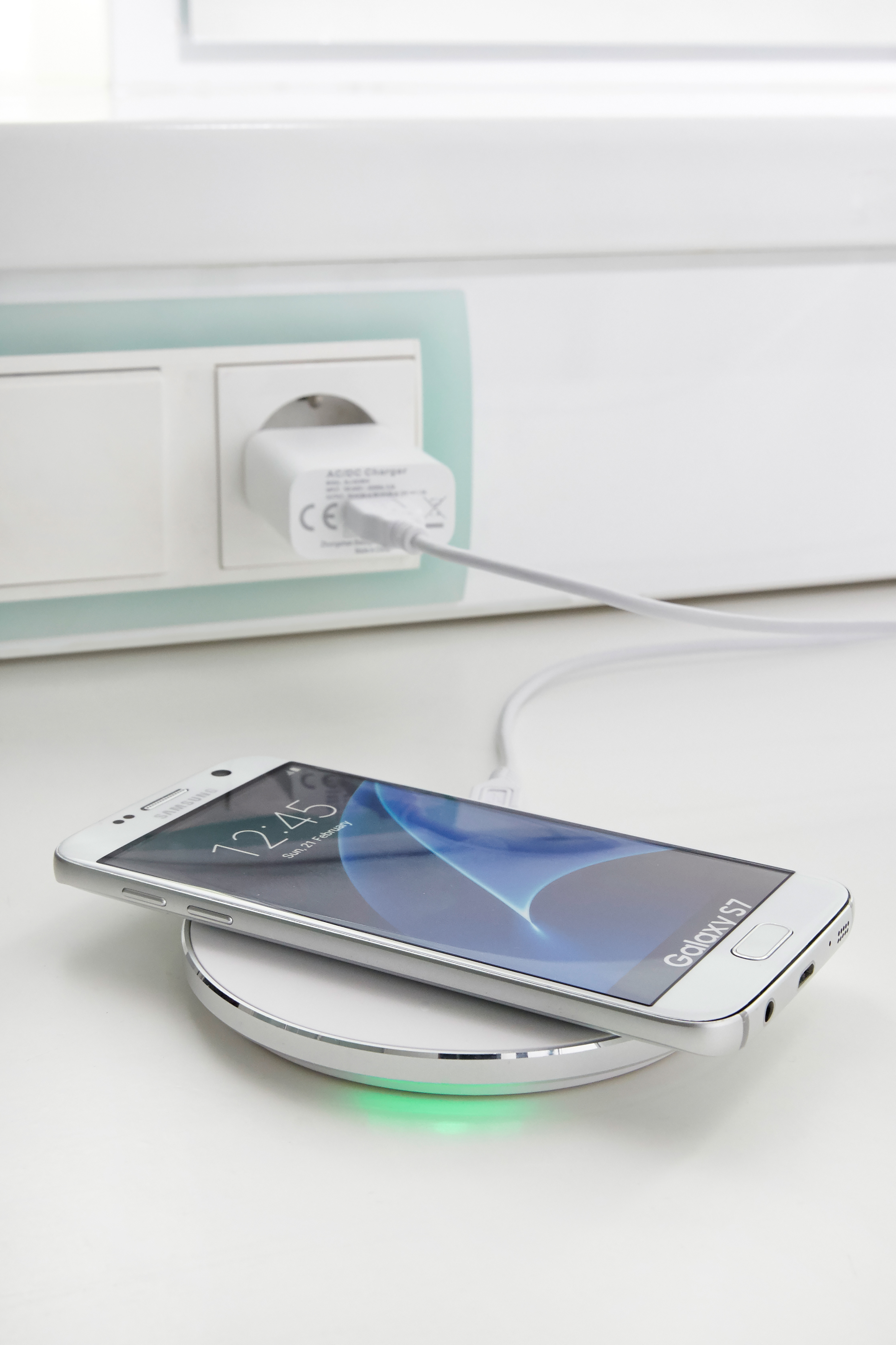 Ein weißes Samsung Galaxy S7 lädt auf einer runden Ladestation. Netzteil steckt in Steckdose.