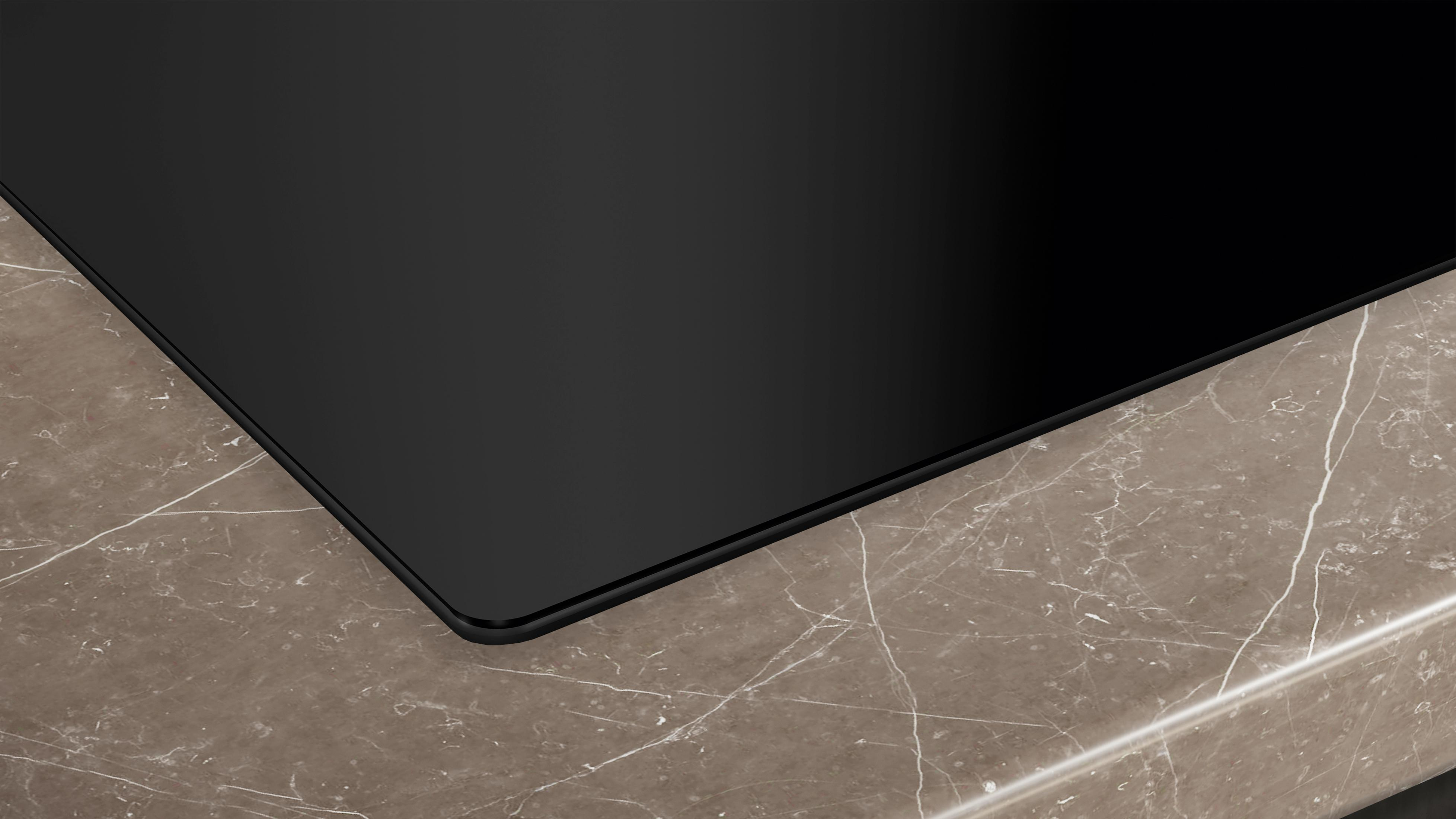 Błyszcząca czarna płyta grzewcza na brązowym blacie marmurowym.