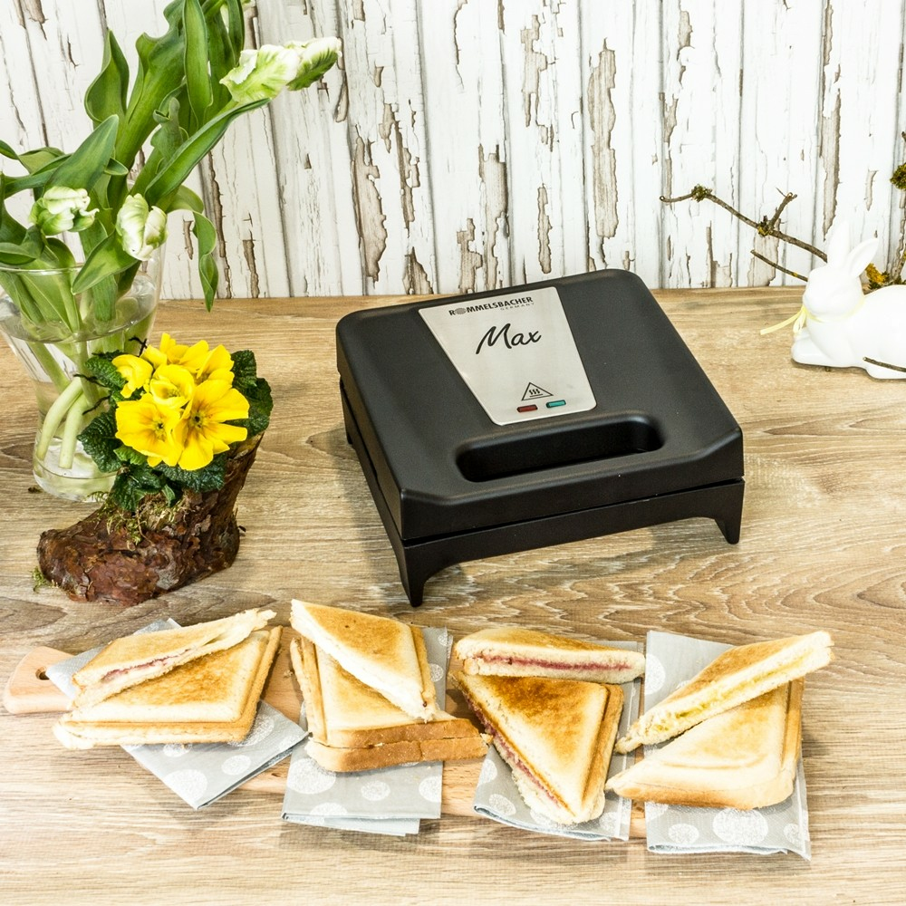 Una sandwichera negra está sobre una mesa de madera con rebanadas de pan tostado cerca.