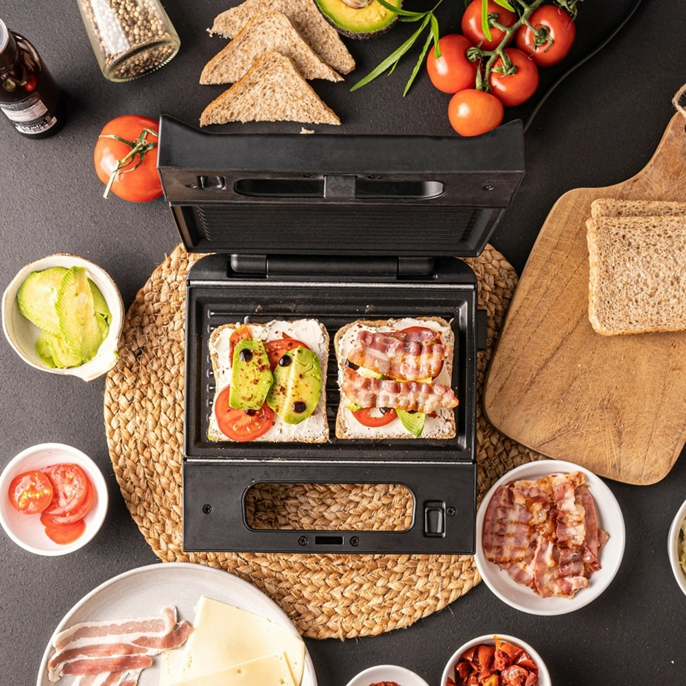 Sandwichera con dos sándwiches abiertos, ingredientes como aguacate, tomates, tocino.