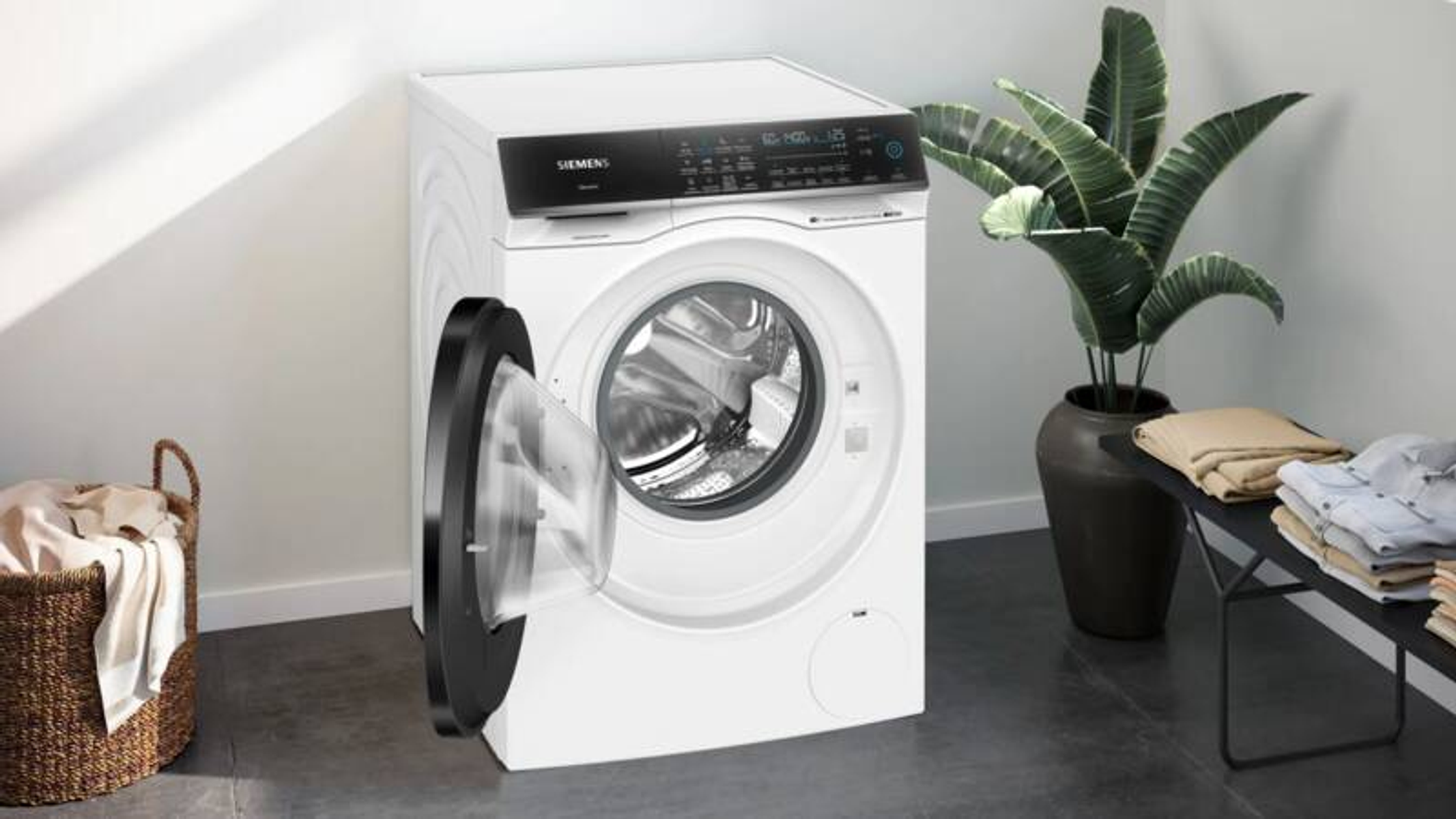 Eine weiße Siemens-Waschmaschine mit offener Tür, daneben ein Wäschekorb und gefaltete Kleidung.