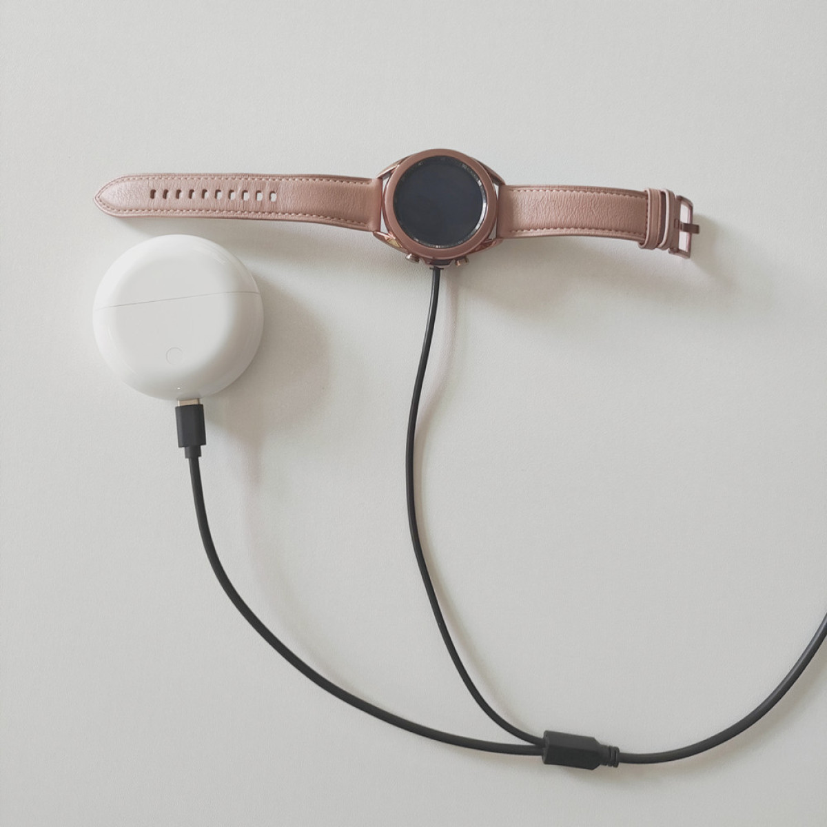 Eine roségoldene Smartwatch mit Lederarmband lädt neben einer weißen Ladestation.