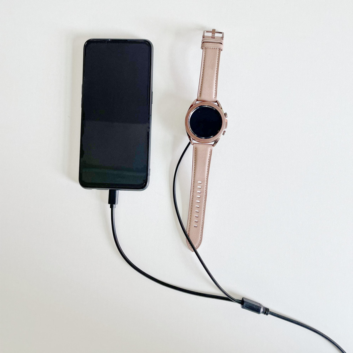 Ein schwarzes Smartphone und eine roségoldene Smartwatch sind mit Kabeln verbunden.