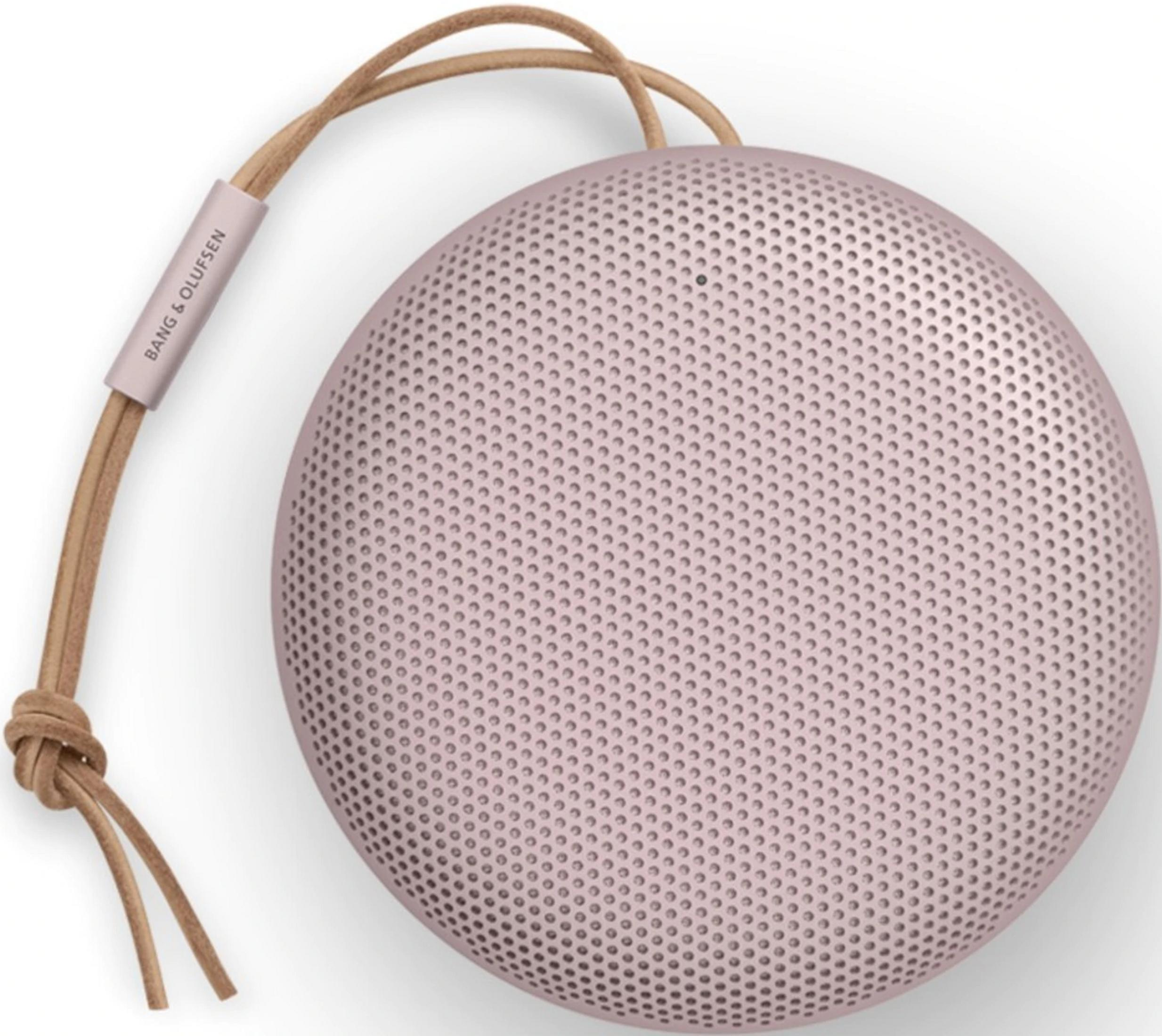 Okrągły, pudrowo-różowy głośnik ze skórzanym paskiem i logo B&O.