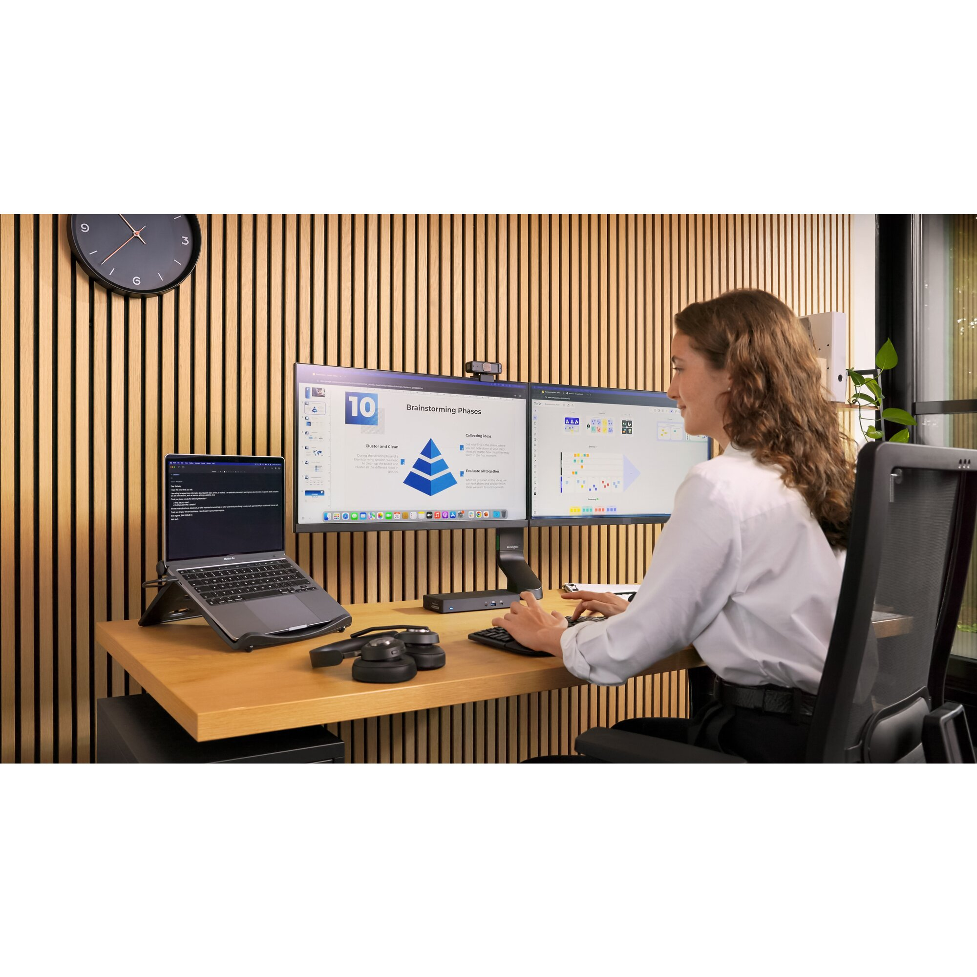 Woman works at a desk with two monitors and a laptop.