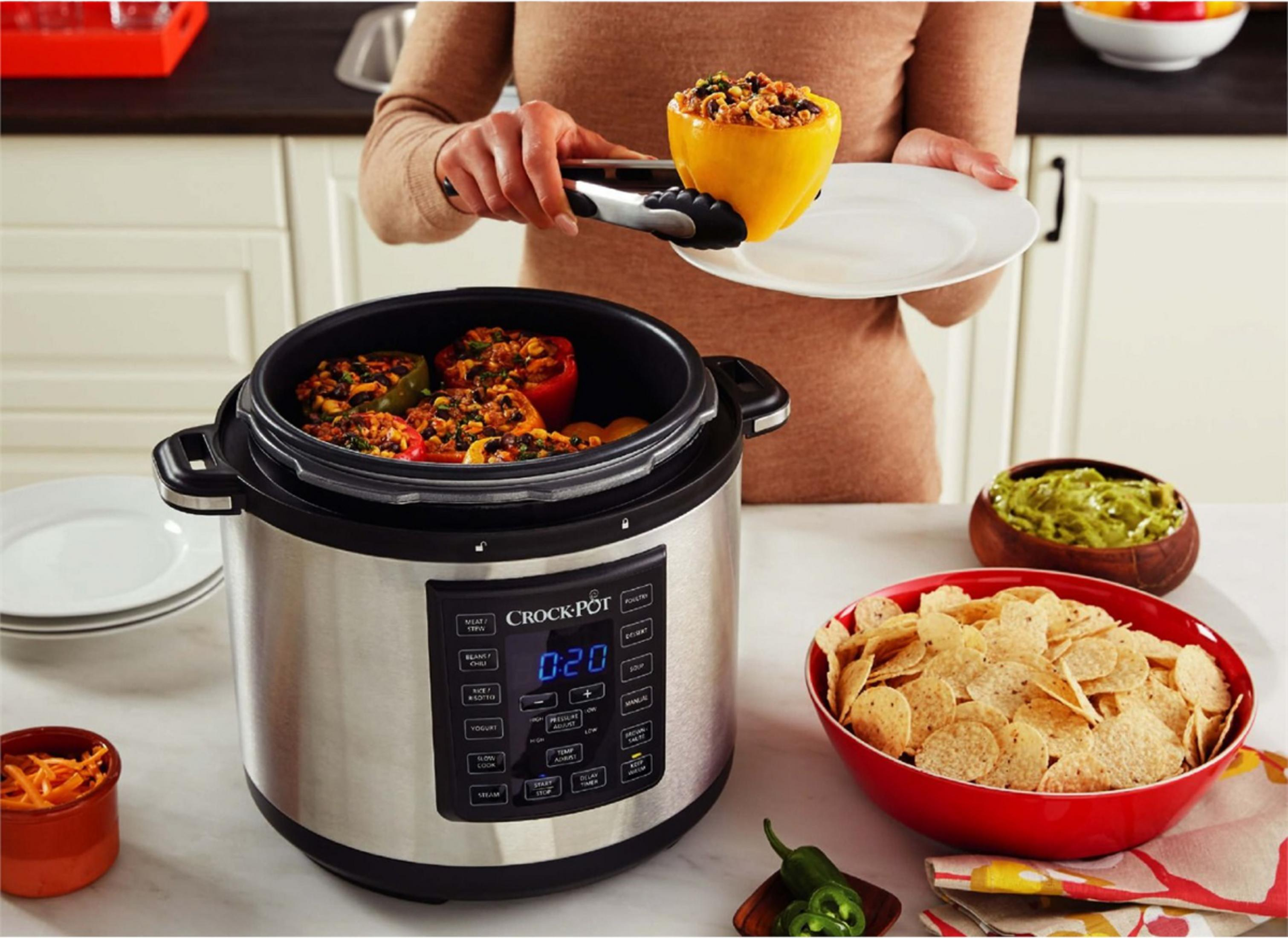 Una persona pone pimientos rellenos en una olla de cocción lenta. Hay totopos y guacamole cerca.