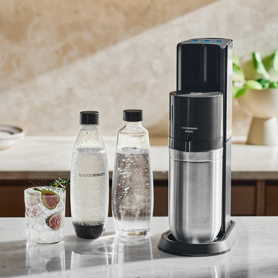 Ein Sodastream-Gerät mit zwei Flaschen und einem Glas Sprudelwasser mit Früchten.