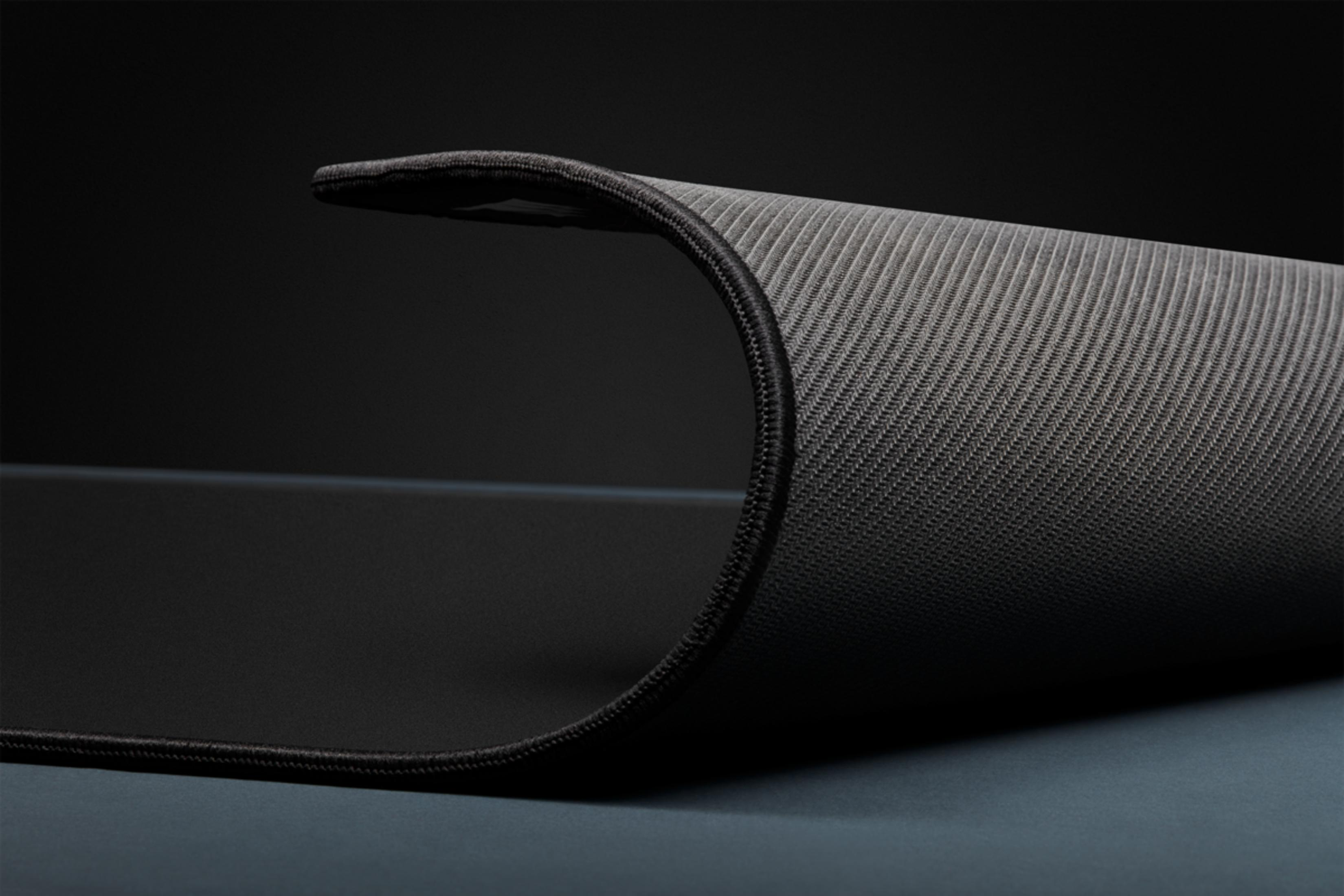 Zbliżenie czarnej podkładki pod mysz z zakrzywioną krawędzią, szarą tkaniną i czarnym szwem.