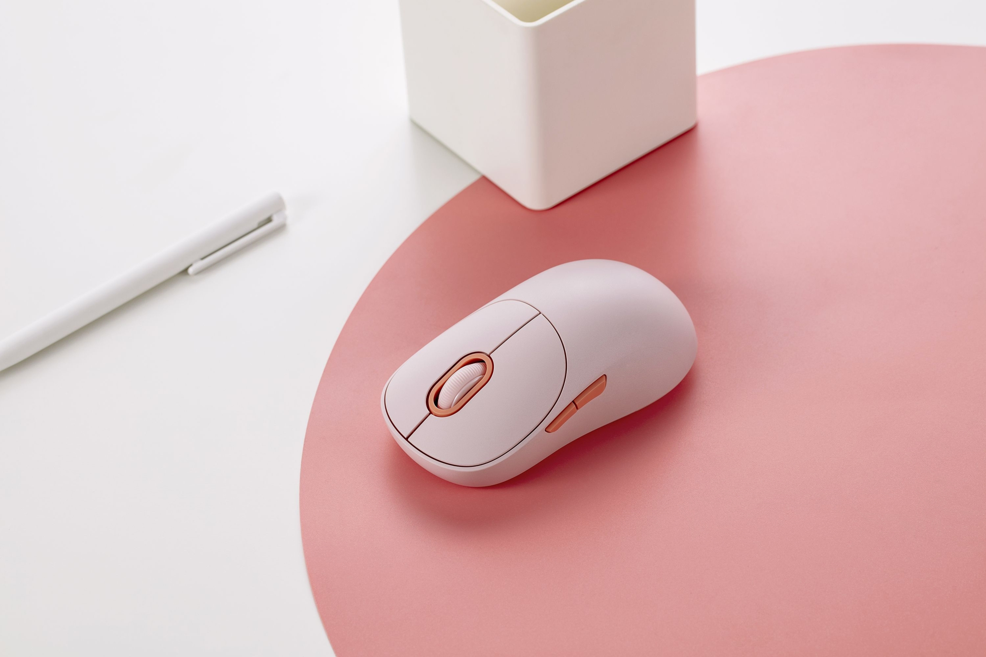 Un mouse per computer rosa chiaro con rotella oro rosa su un tappetino rosa accanto a una penna bianca.