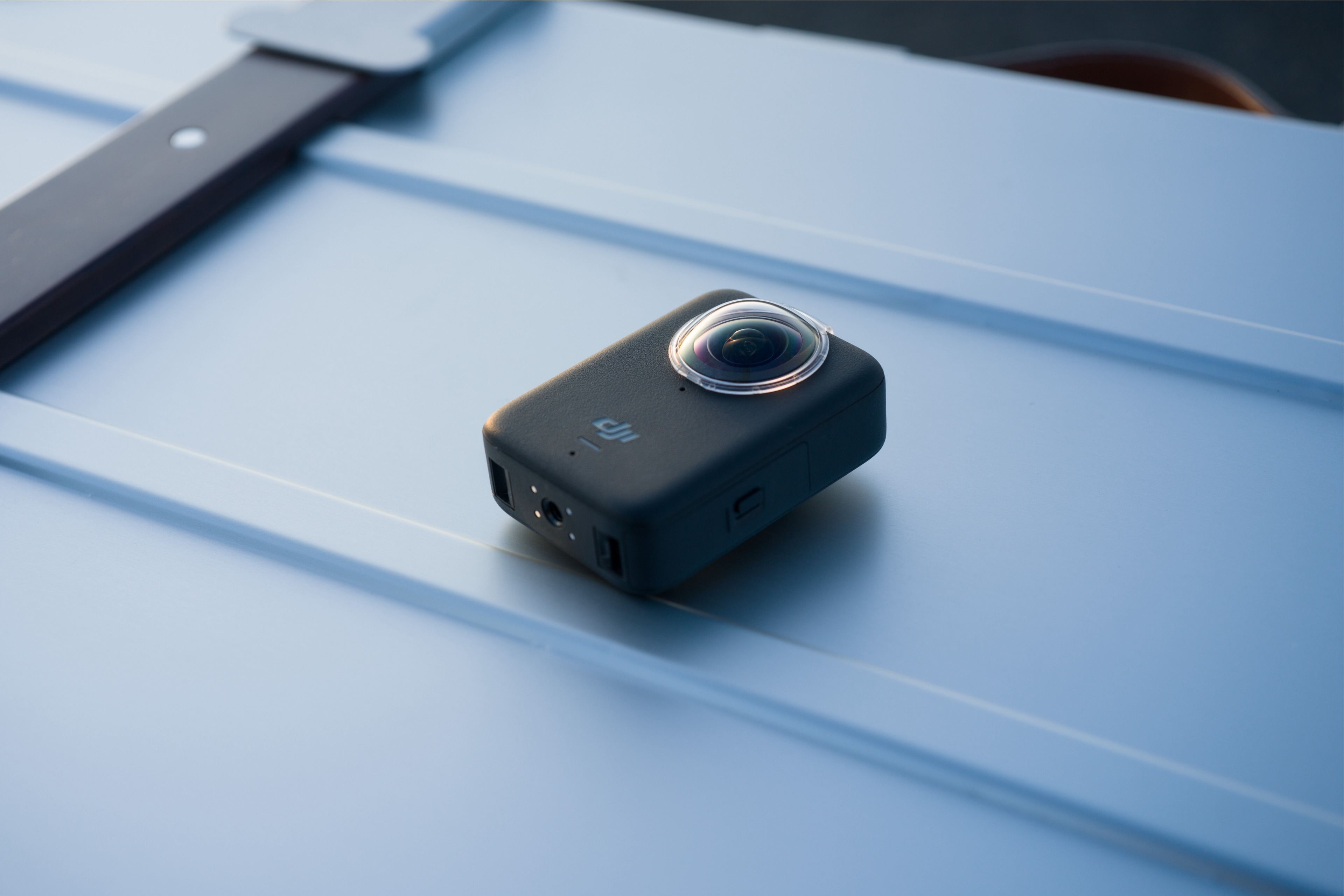 Una fotocamera nera a 360 gradi poggia su una superficie blu.