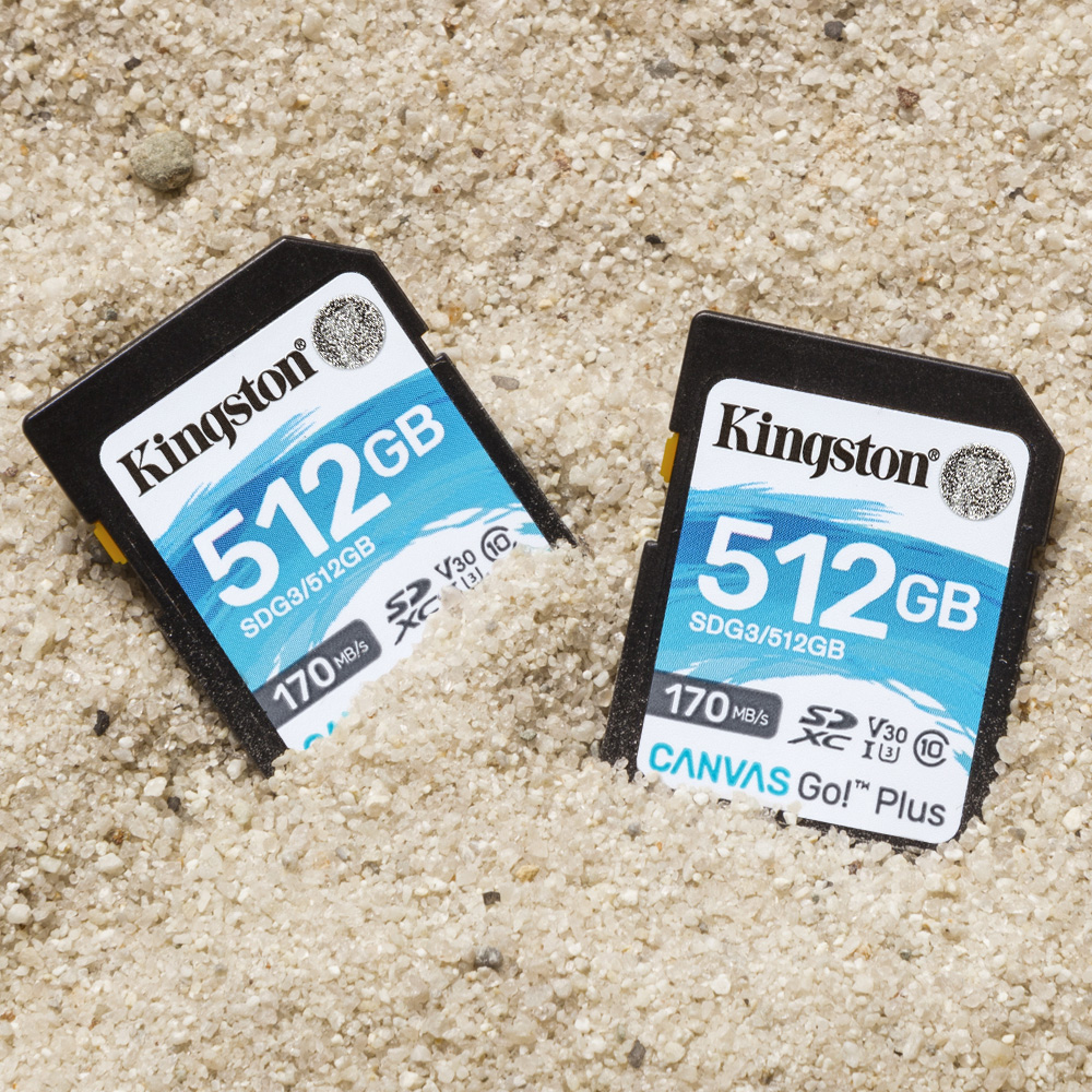 Dos tarjetas SD Kingston de 512GB enterradas en arena, mostrando capacidad y velocidad.